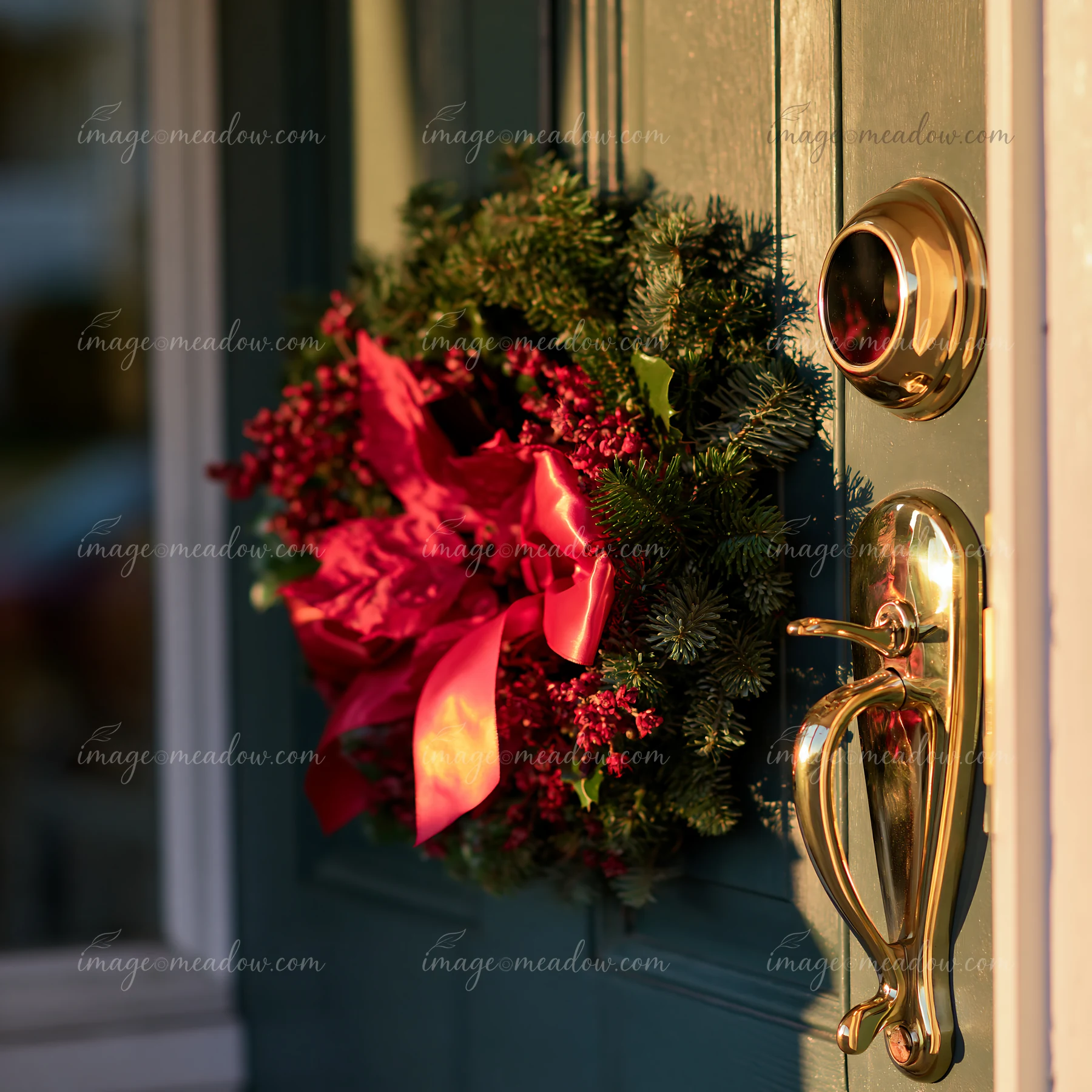 A Christmas wreath with red decorations hangs on a green apartment door beside a shiny gold handle.