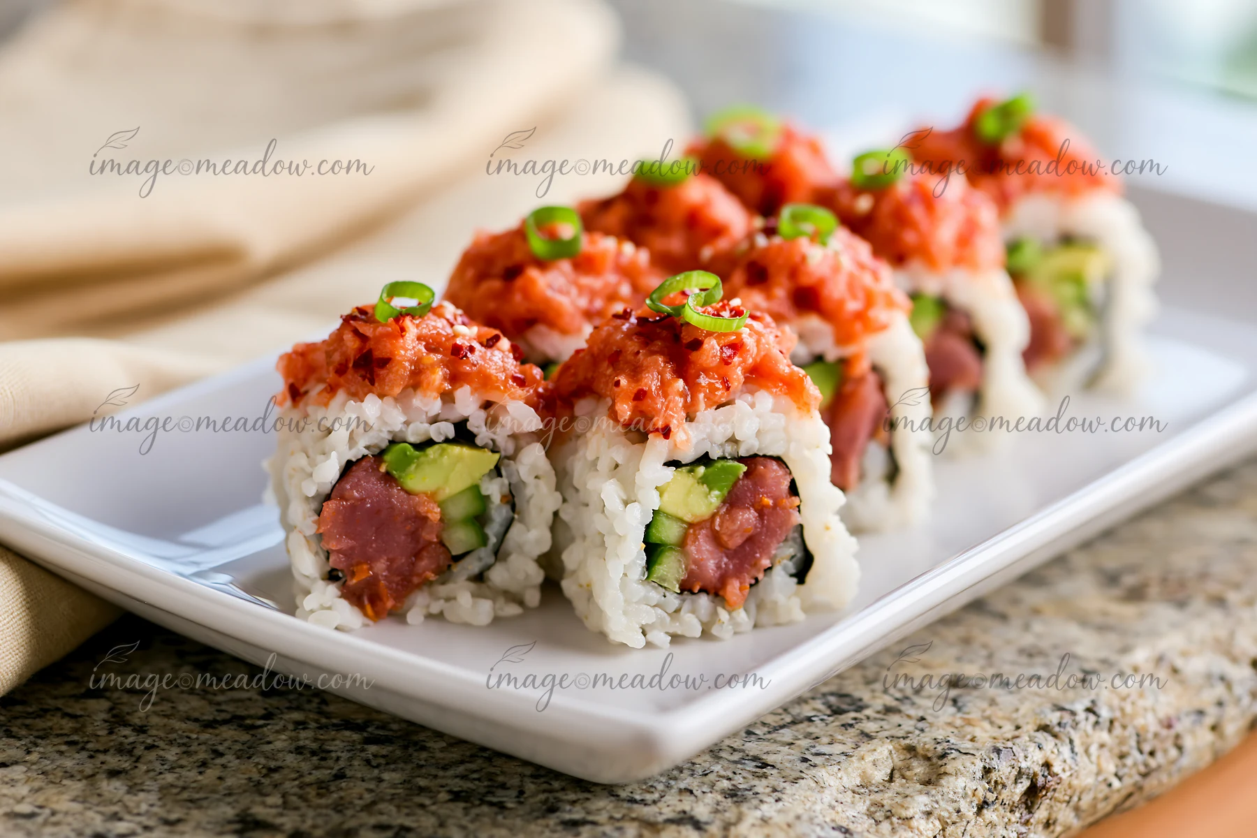 A close-up view of a plate containing several spicy tuna rolls, showing layers of sushi rice, avocado, and topped with spicy tuna.
