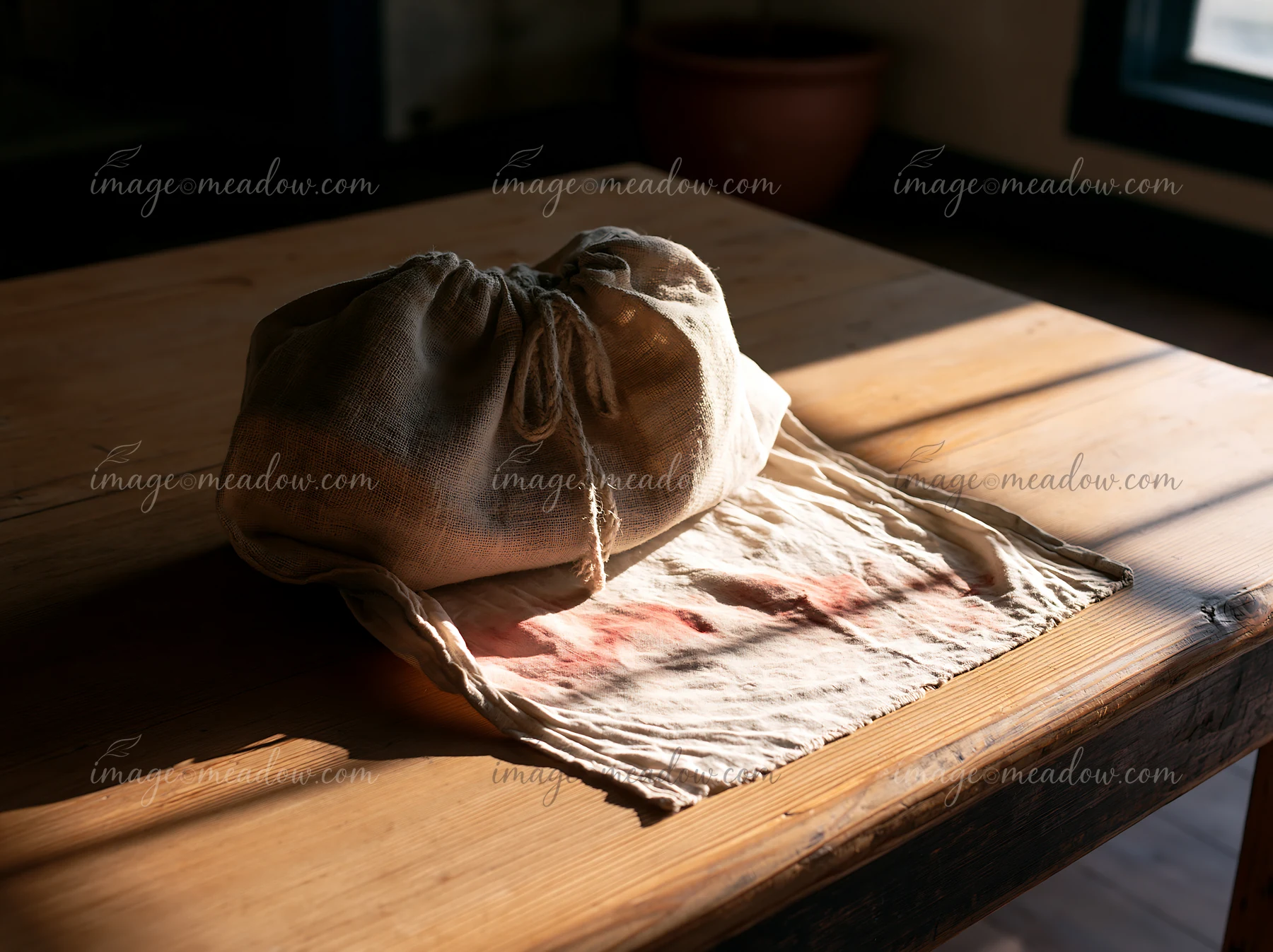 A cloth bag rests on a table, revealing red pigment stains on the rough textile underneath.
