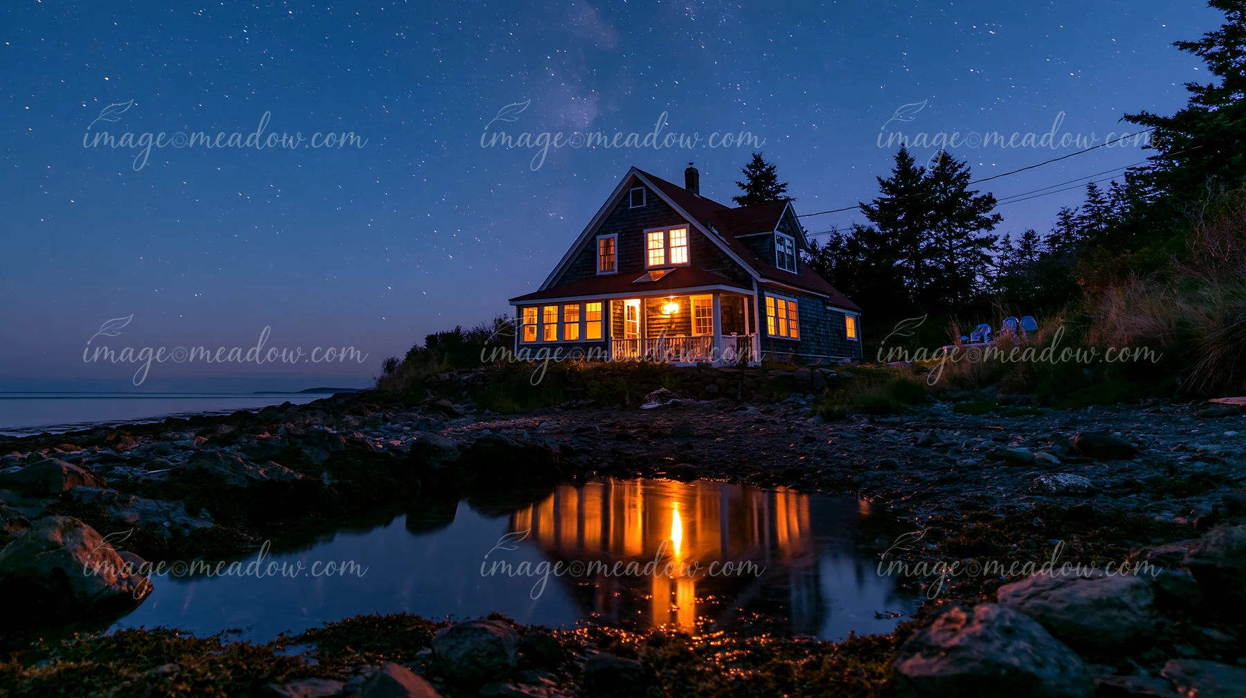 A coastal home stands by the shore, reflecting light in calm water.