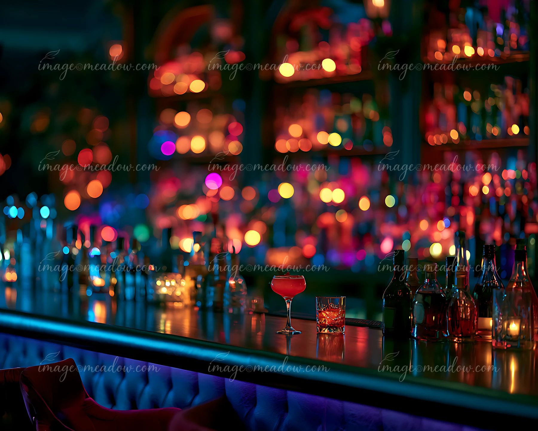 A cocktail glass sits on the bar counter amid a vibrant atmosphere filled with colorful lights and a variety of bottles on display.