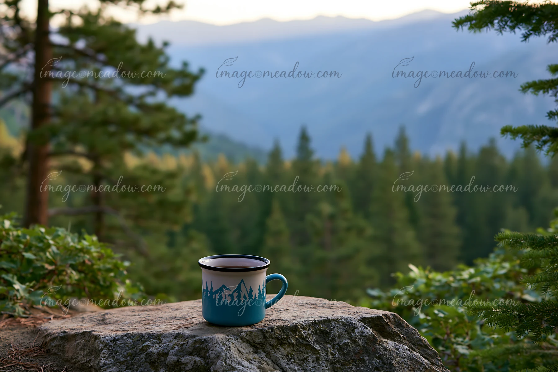 A coffee cup rests on a rock in a pine forest, with a mountain range in the distance.