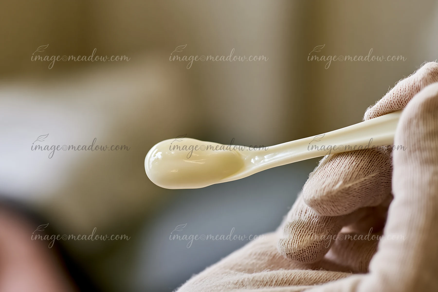 A cosmetic spatula holds a cream dose for skincare use in a well-lit setting.