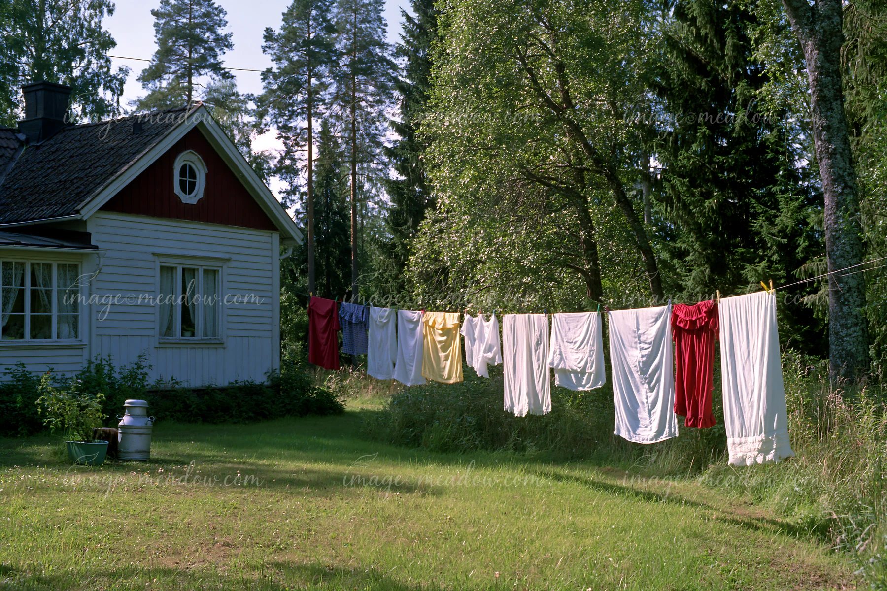A cottage near forest edge features colorful laundry drying on a line.