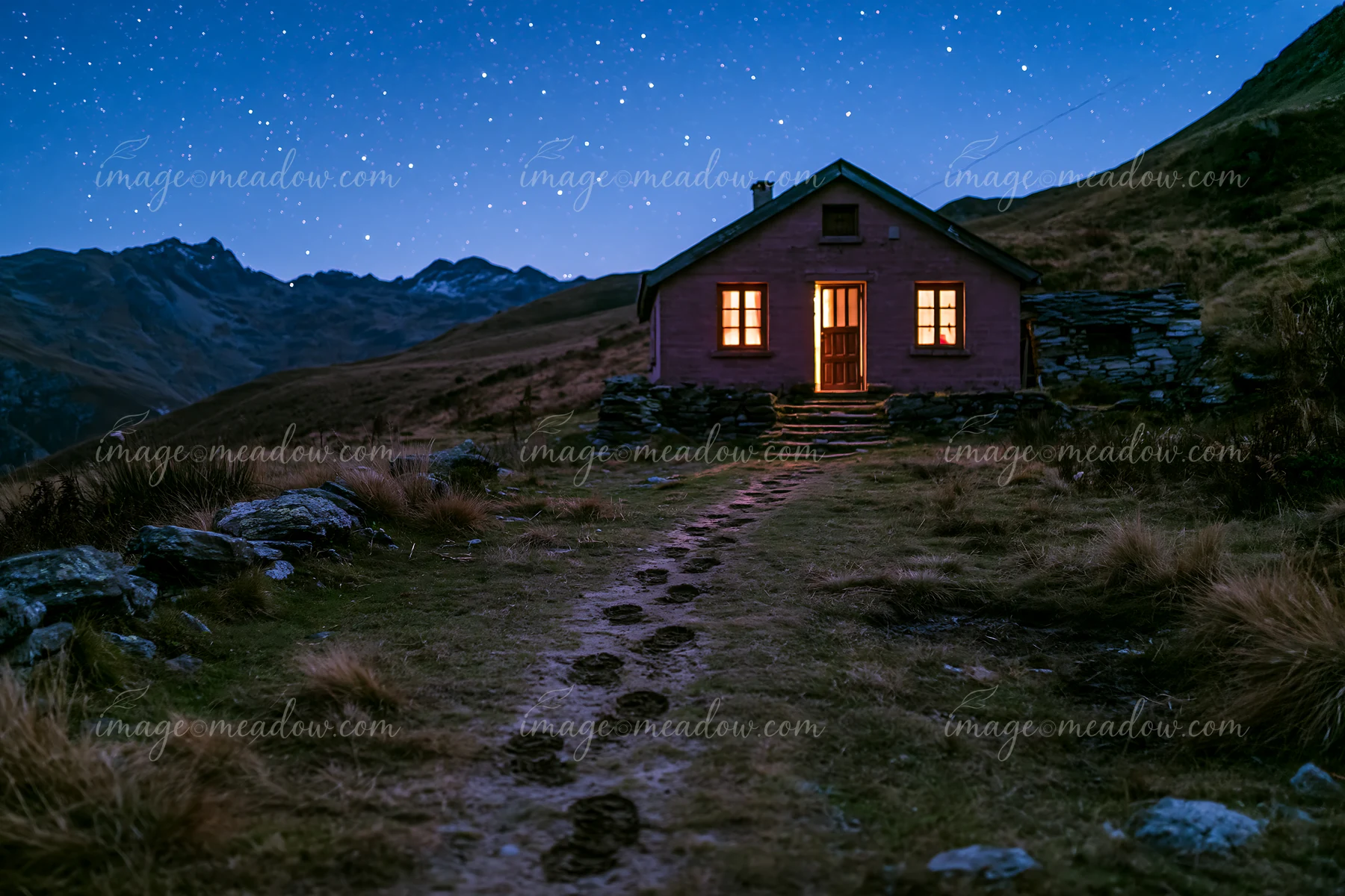 A cottage under stars stands in a mountainous area.