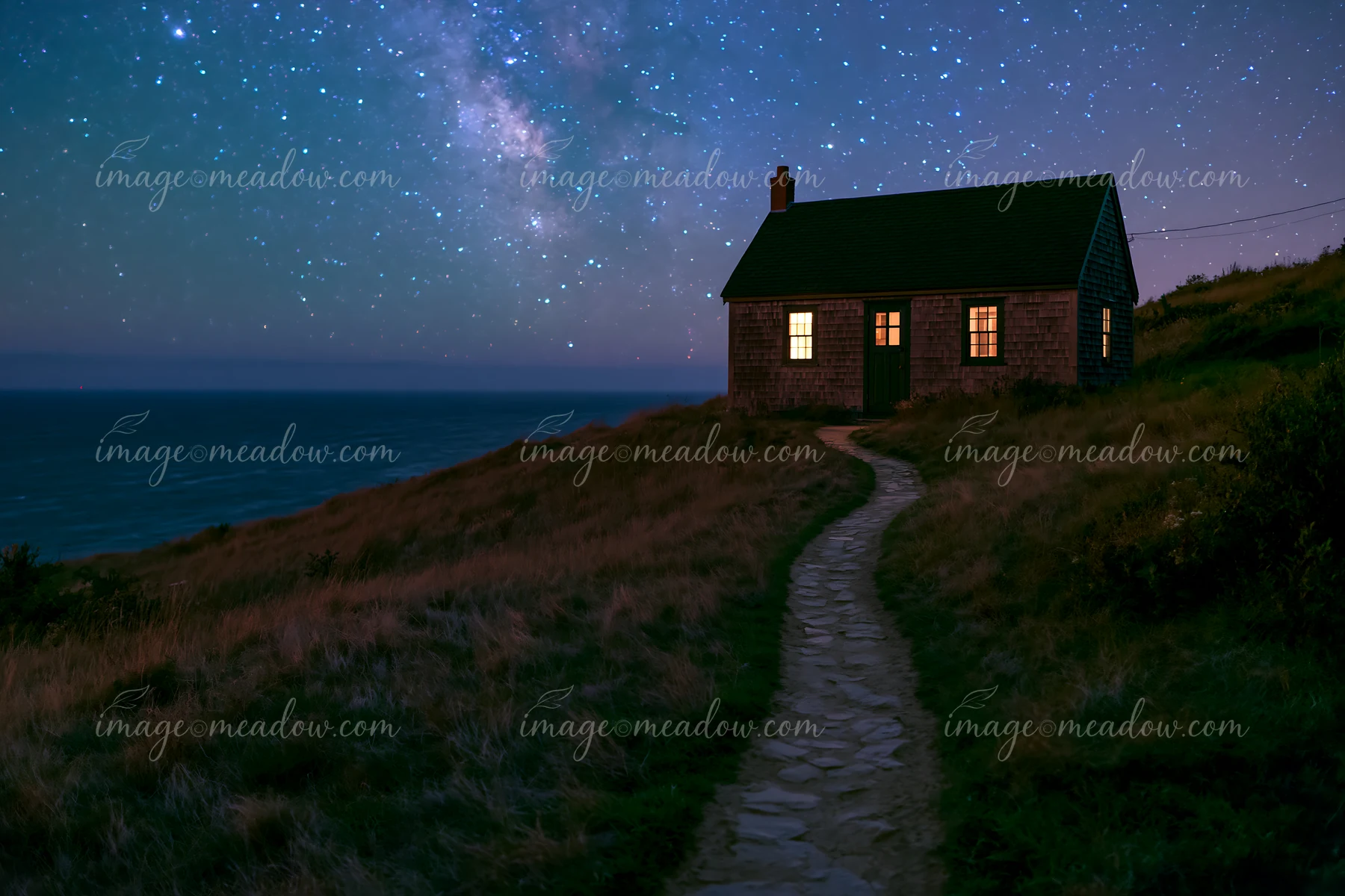 A cottage under stars with a stone path leads to the ocean.