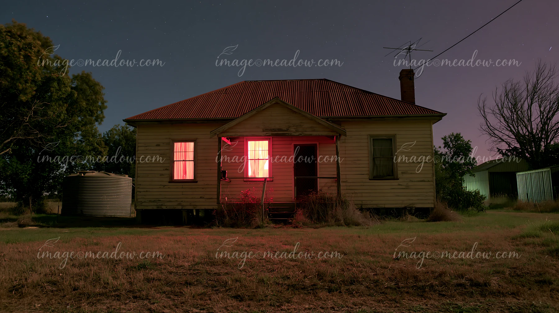 A country home shows warm light from its windows against a clear night sky.