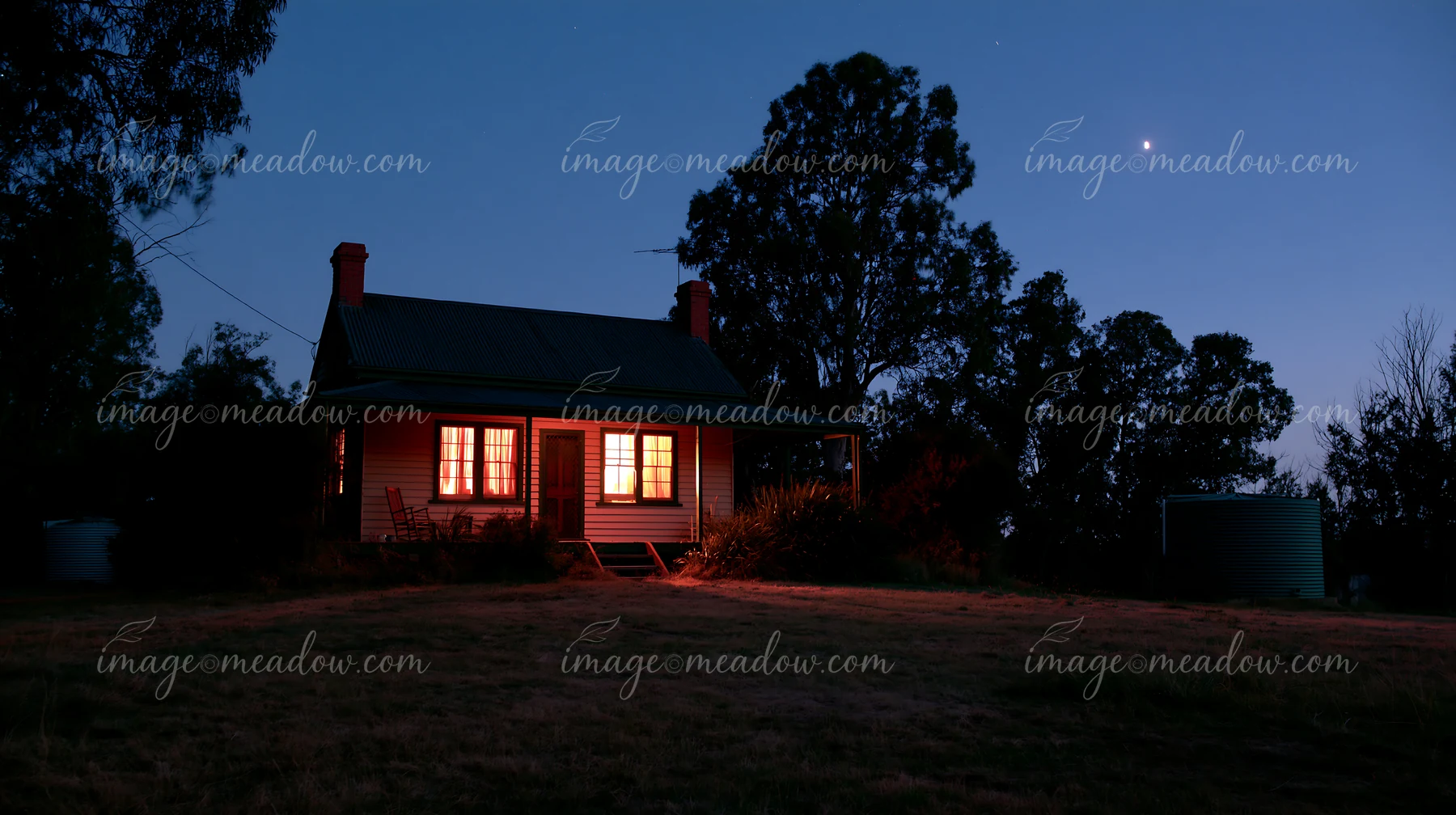 A country home stands under a clear night sky with a bright moon shining above.