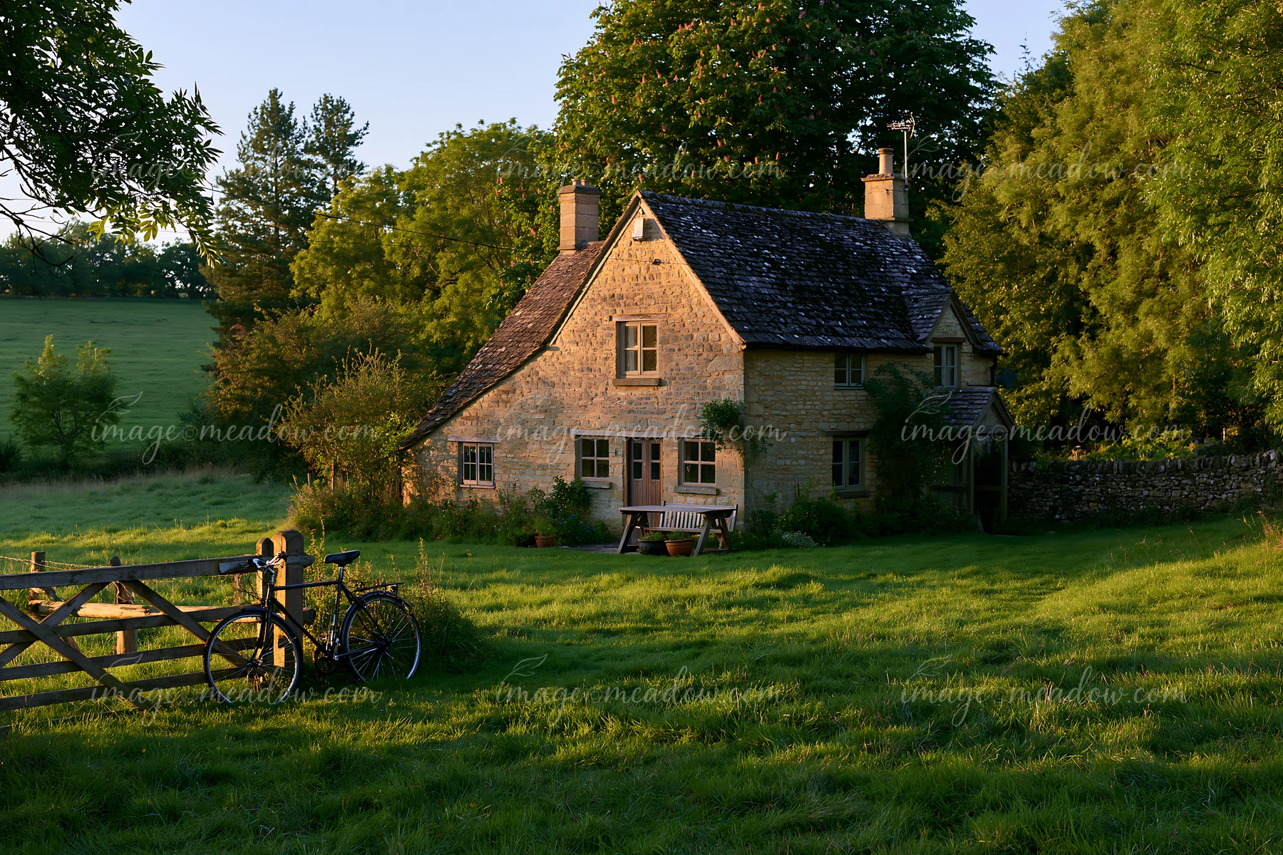 A country home with bicycle outside is set in a green field during golden hour.