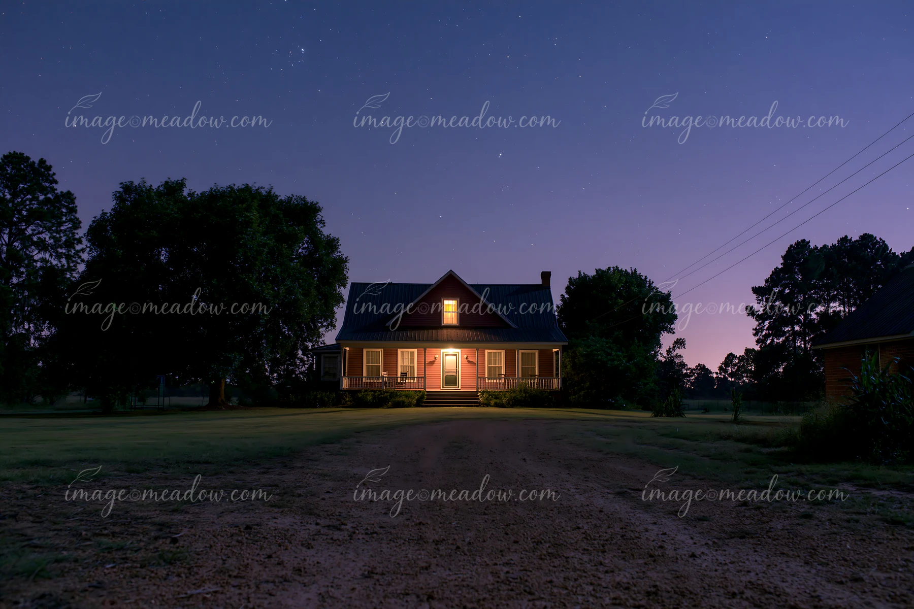 A country house stands alone in a field, lit warmly from within, under a starry sky.