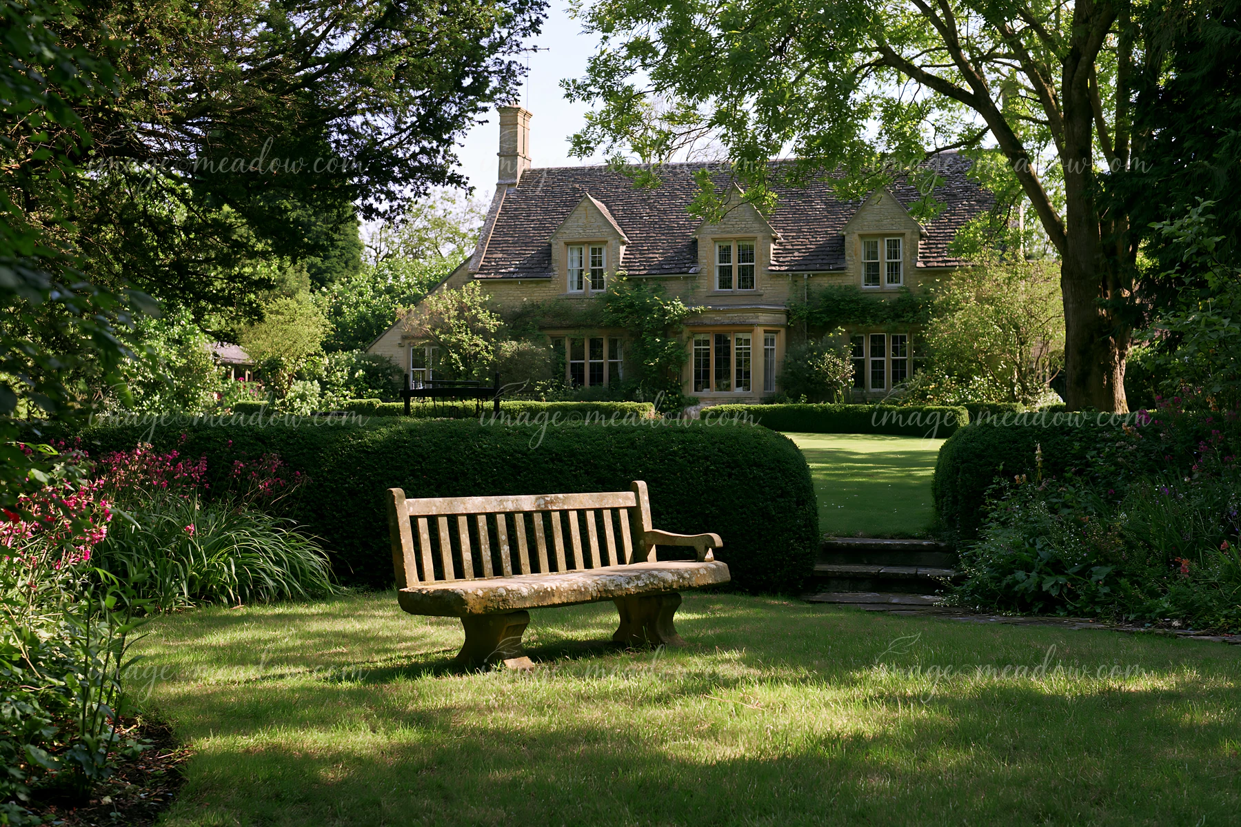 A country house surrounded by hedges stands in a well-kept garden.