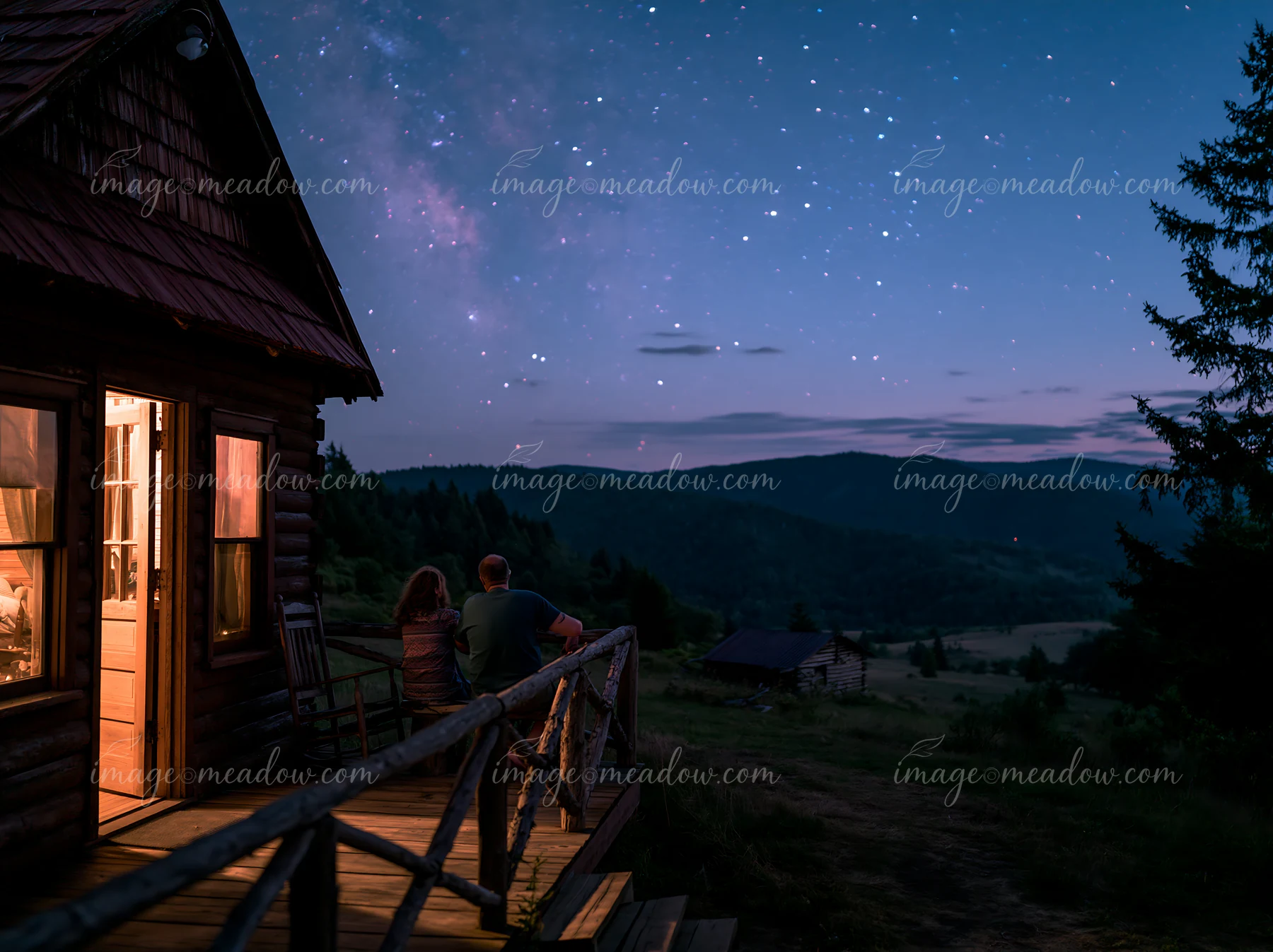 A couple beside a mountain cabin under stars enjoys the night sky and the landscape.