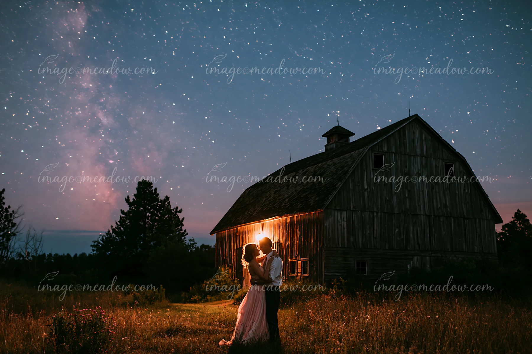 A couple dances together under a starry sky beside an old barn.