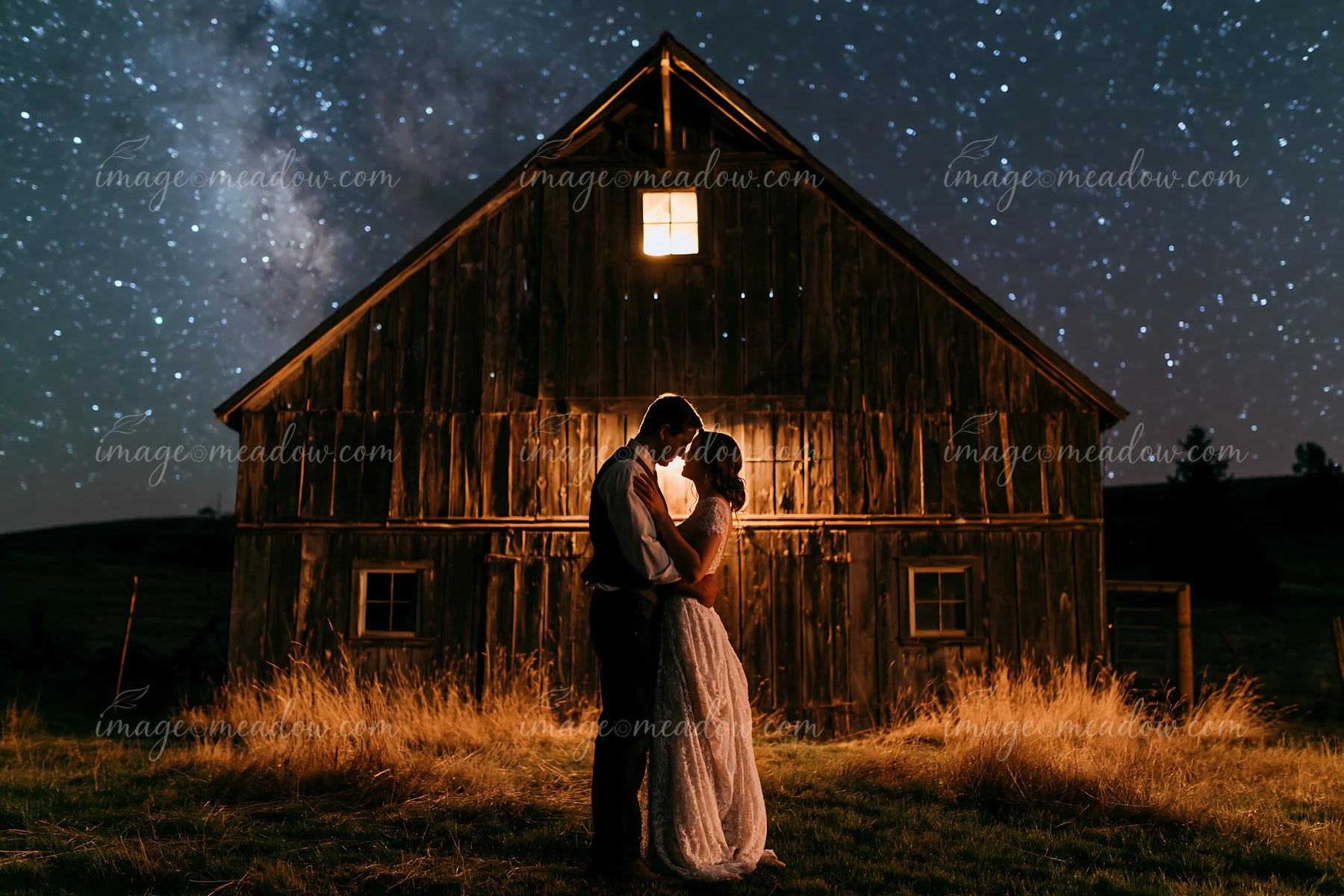 A couple dancing under stars outdoors stands in front of a rustic barn.