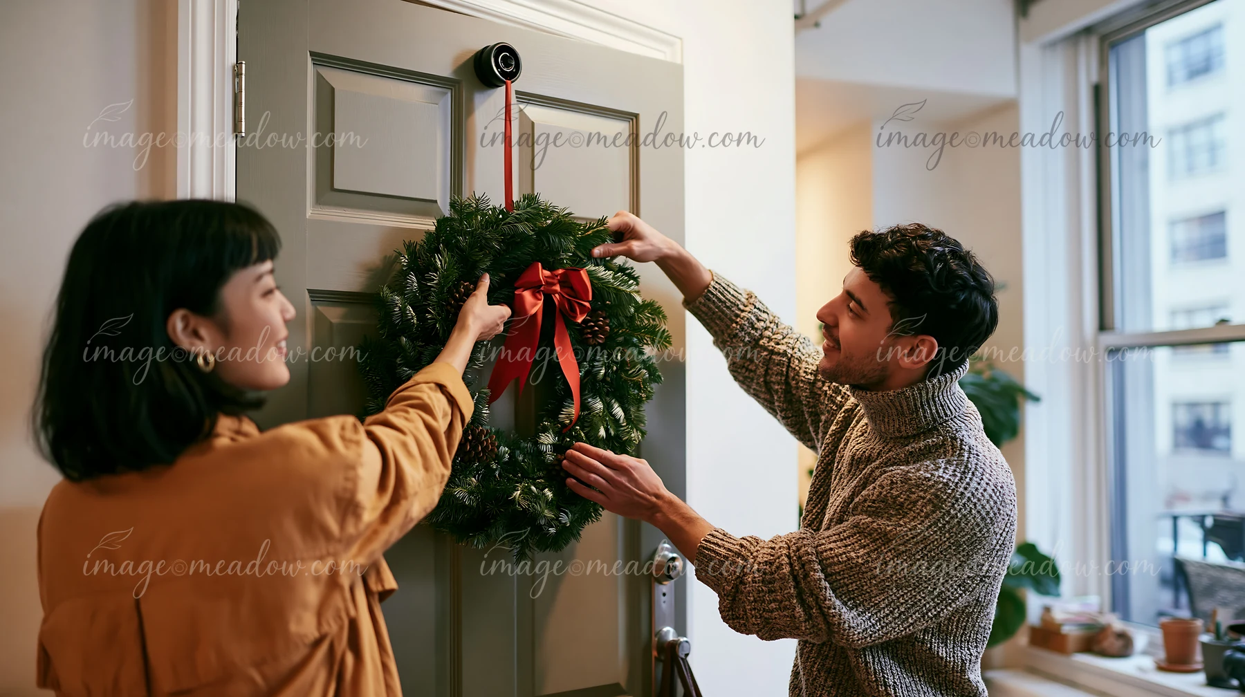 A couple decorates their apartment door with a Christmas wreath, adding a festive touch.