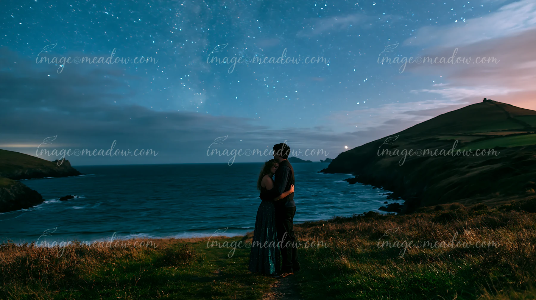 A couple embracing under a starry sky near the ocean.