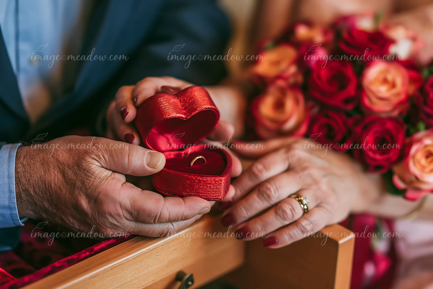 A couple is holding a heart-shaped ring box with a ring inside while surrounded by roses.