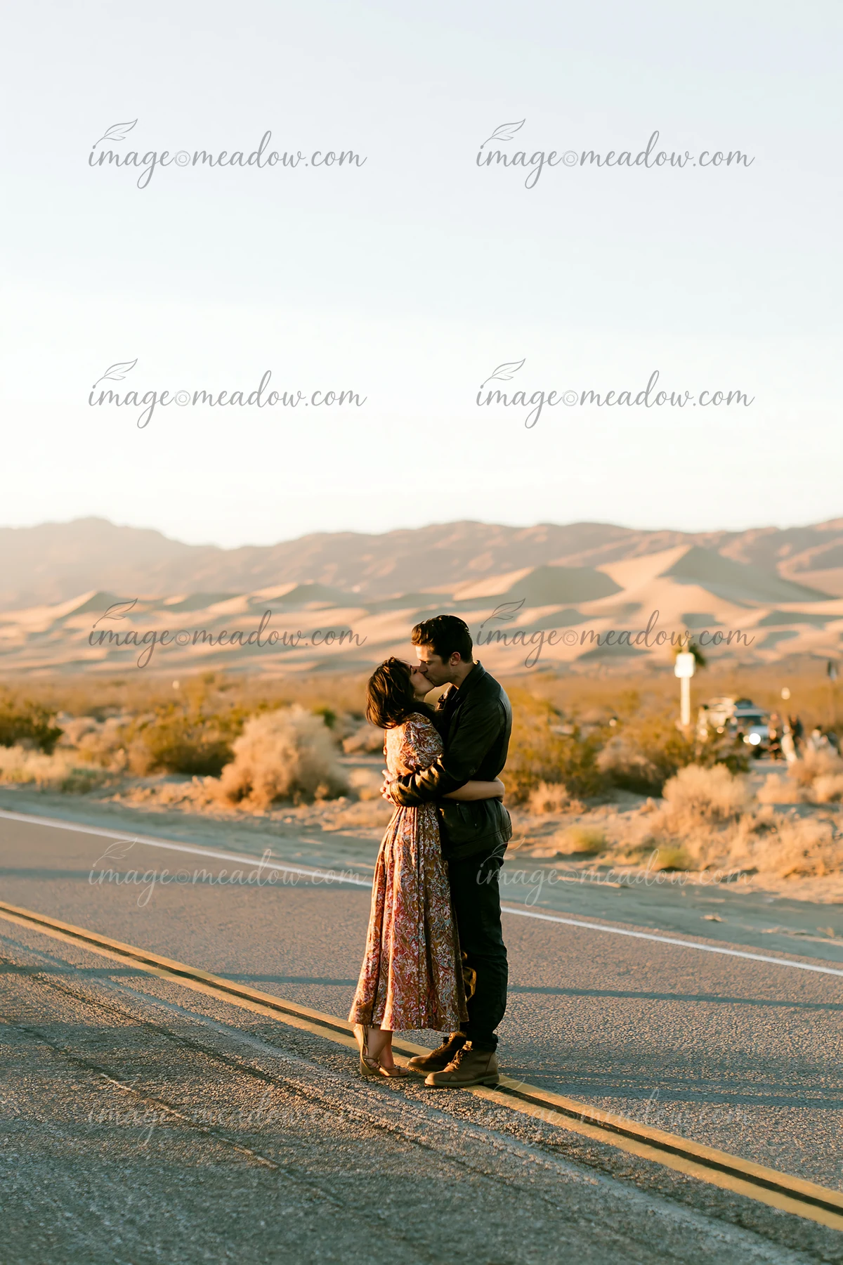 A couple is kissing on a quiet road surrounded by desert terrain at sunset.