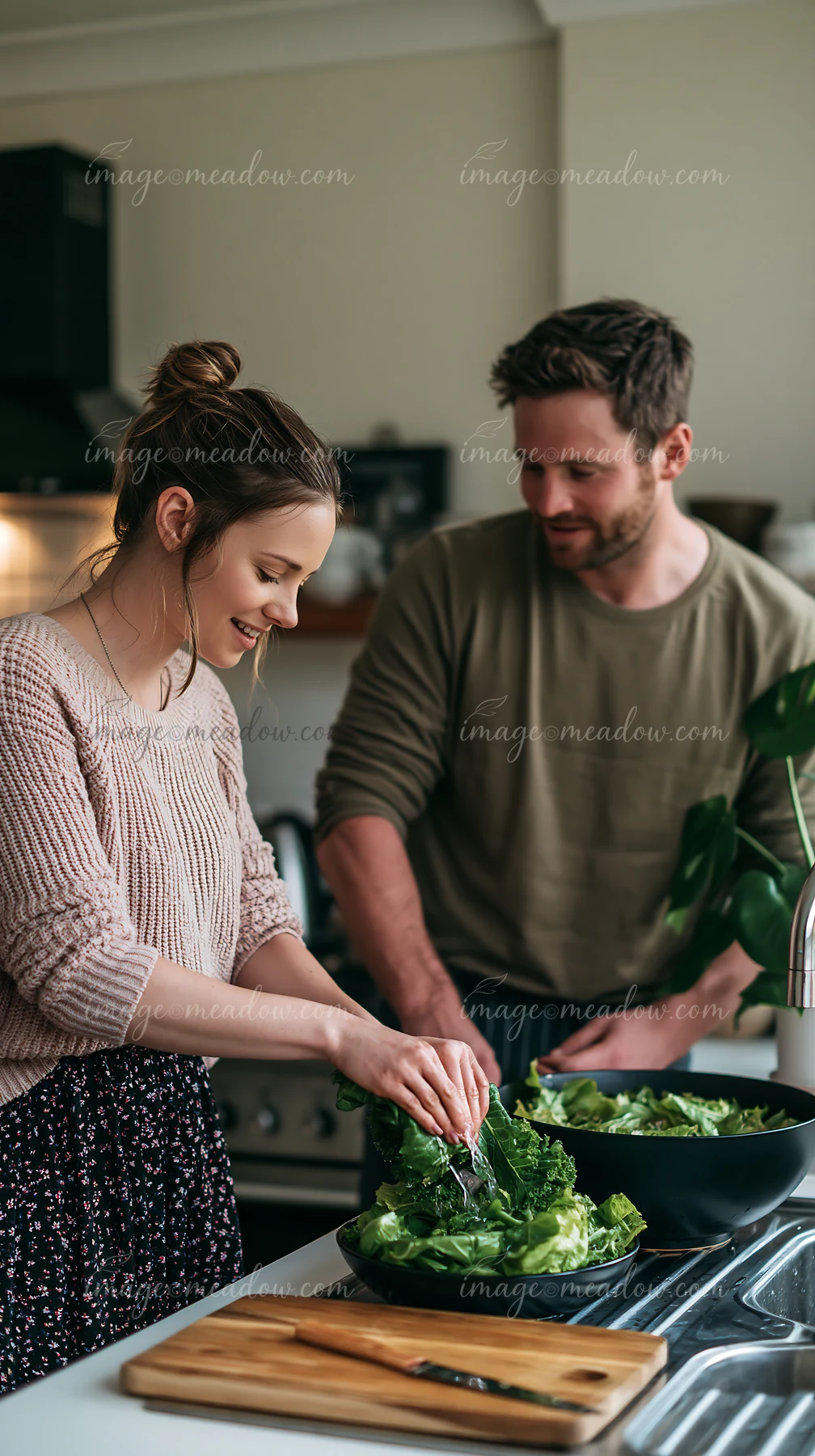 A couple is preparing a salad together in a modern kitchen.