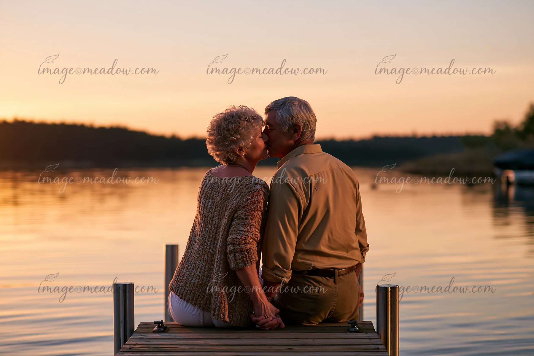 A couple is sitting on a dock by the lake, sharing a kiss at sunset.