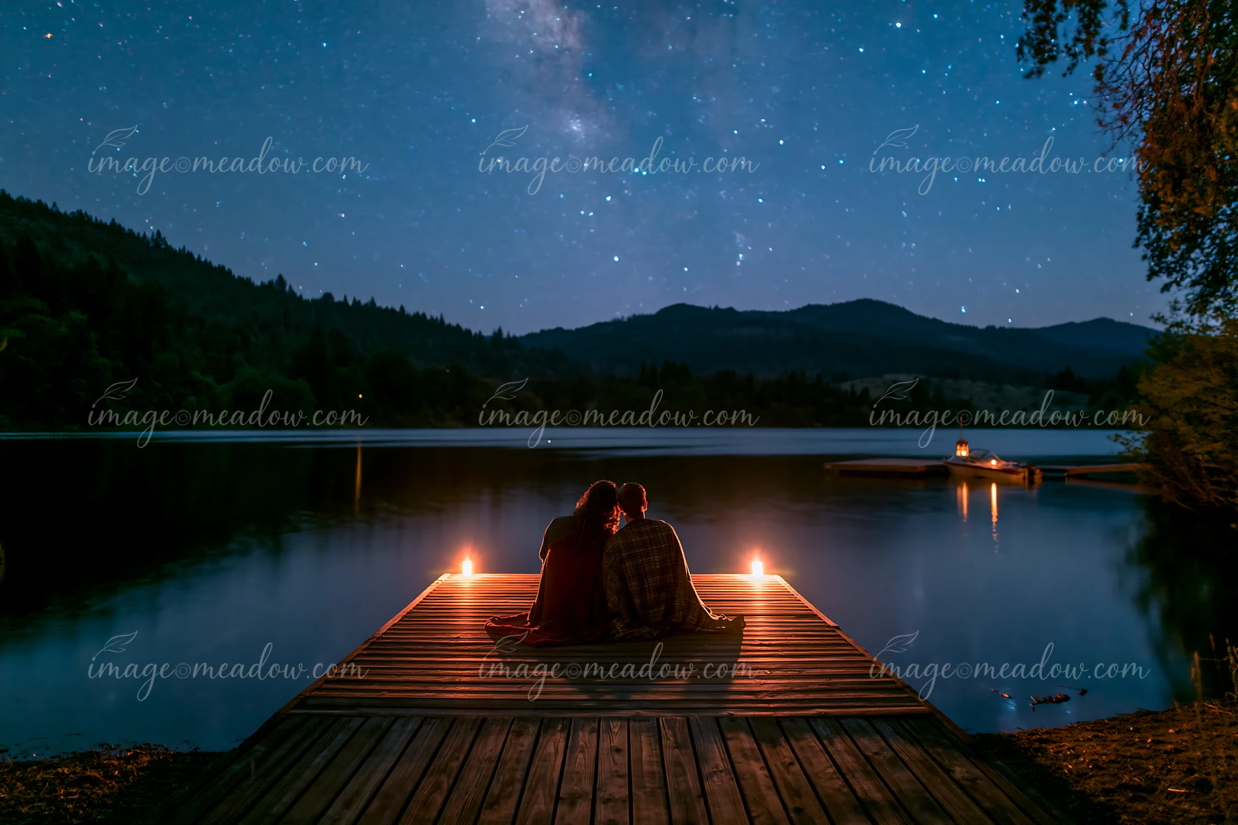 A couple is watching stars beside a lake, sitting on a wooden dock with candles lit around them.