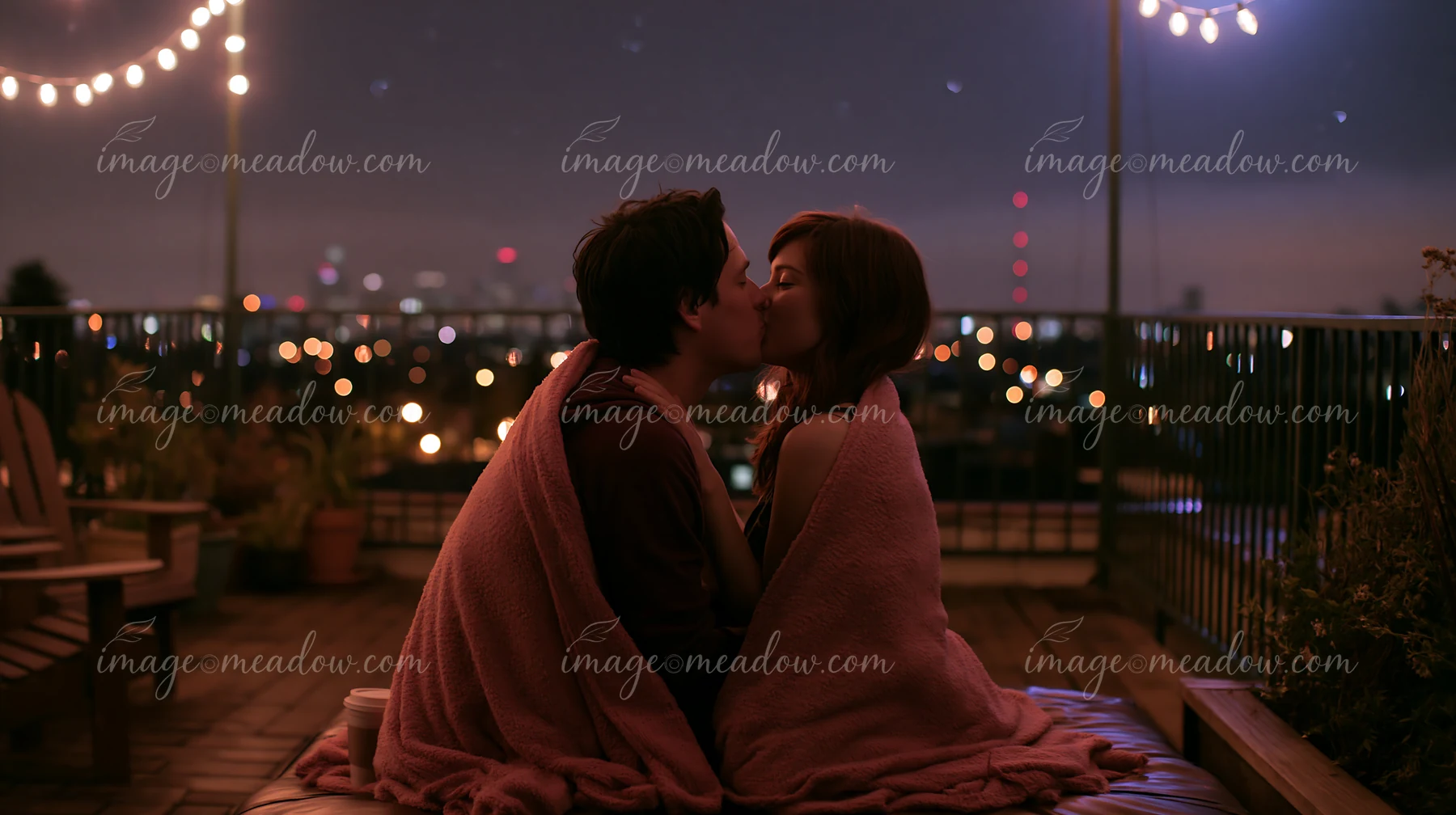 A couple kisses beneath stars while wrapped in blanket on a rooftop.