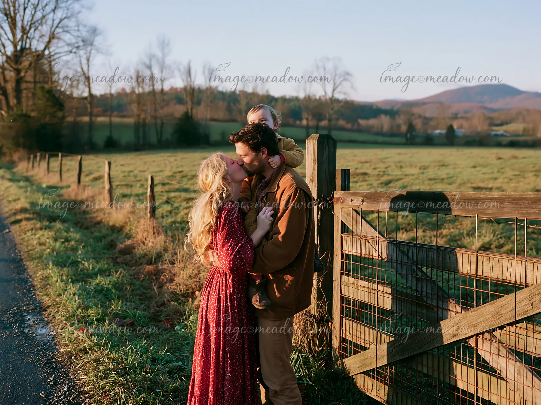 A couple kisses on a country road as a child is held.