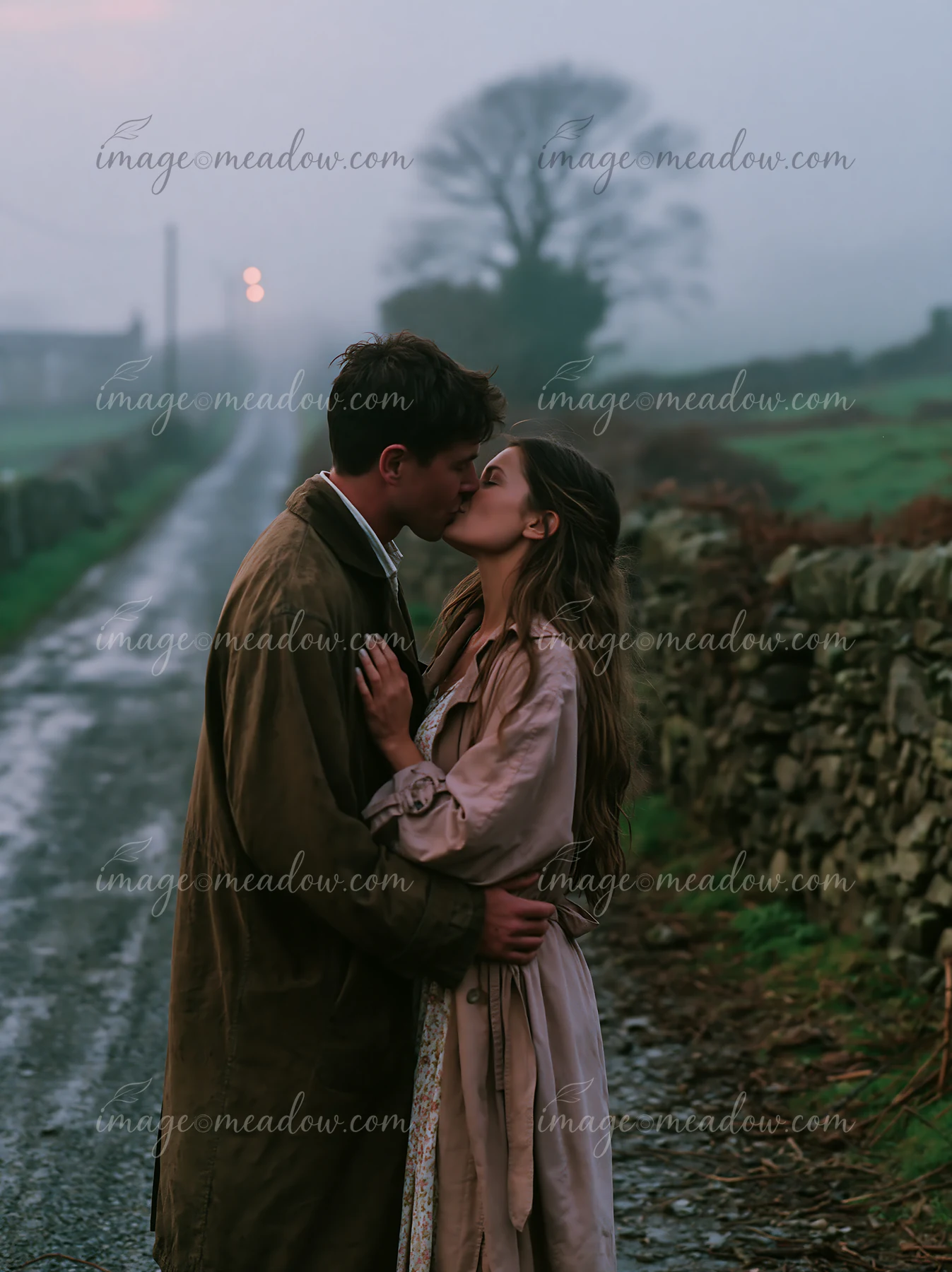 A couple kisses on a country road surrounded by fields and stone walls as fog rolls in.