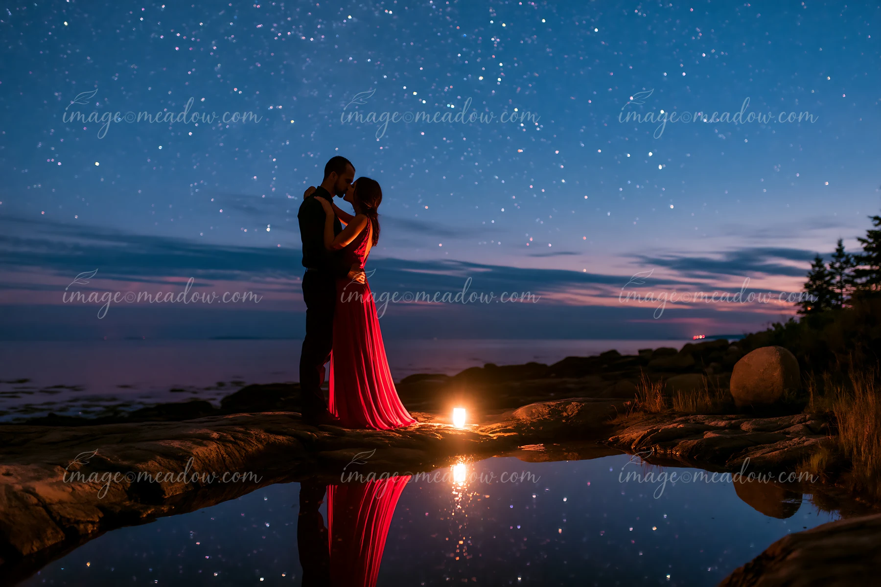 A couple kisses on a rocky shore under a starry night sky, with a gentle glow from a candle reflecting in the water.