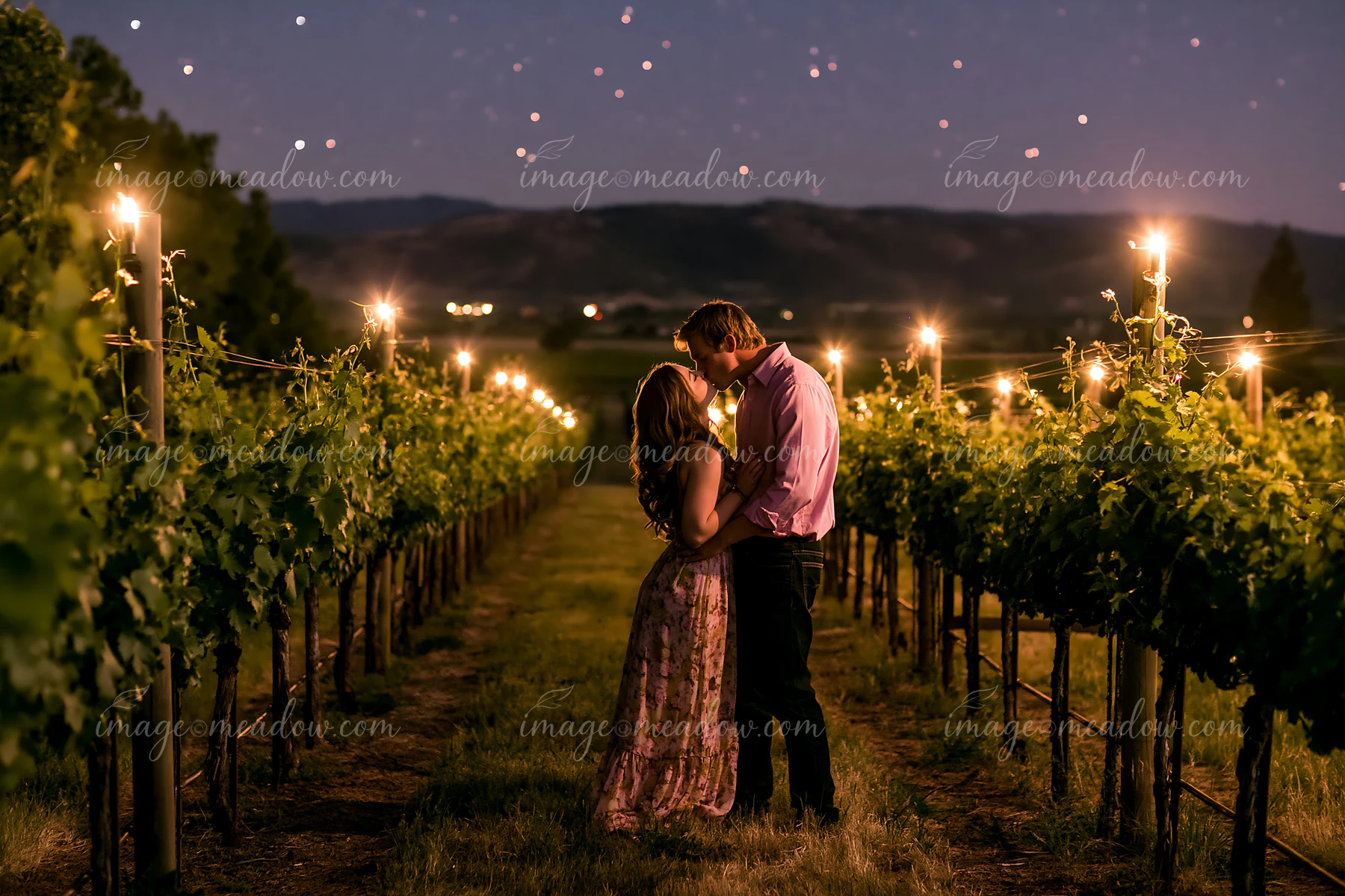 A couple kissing under stars during a romantic date in a vineyard at night.