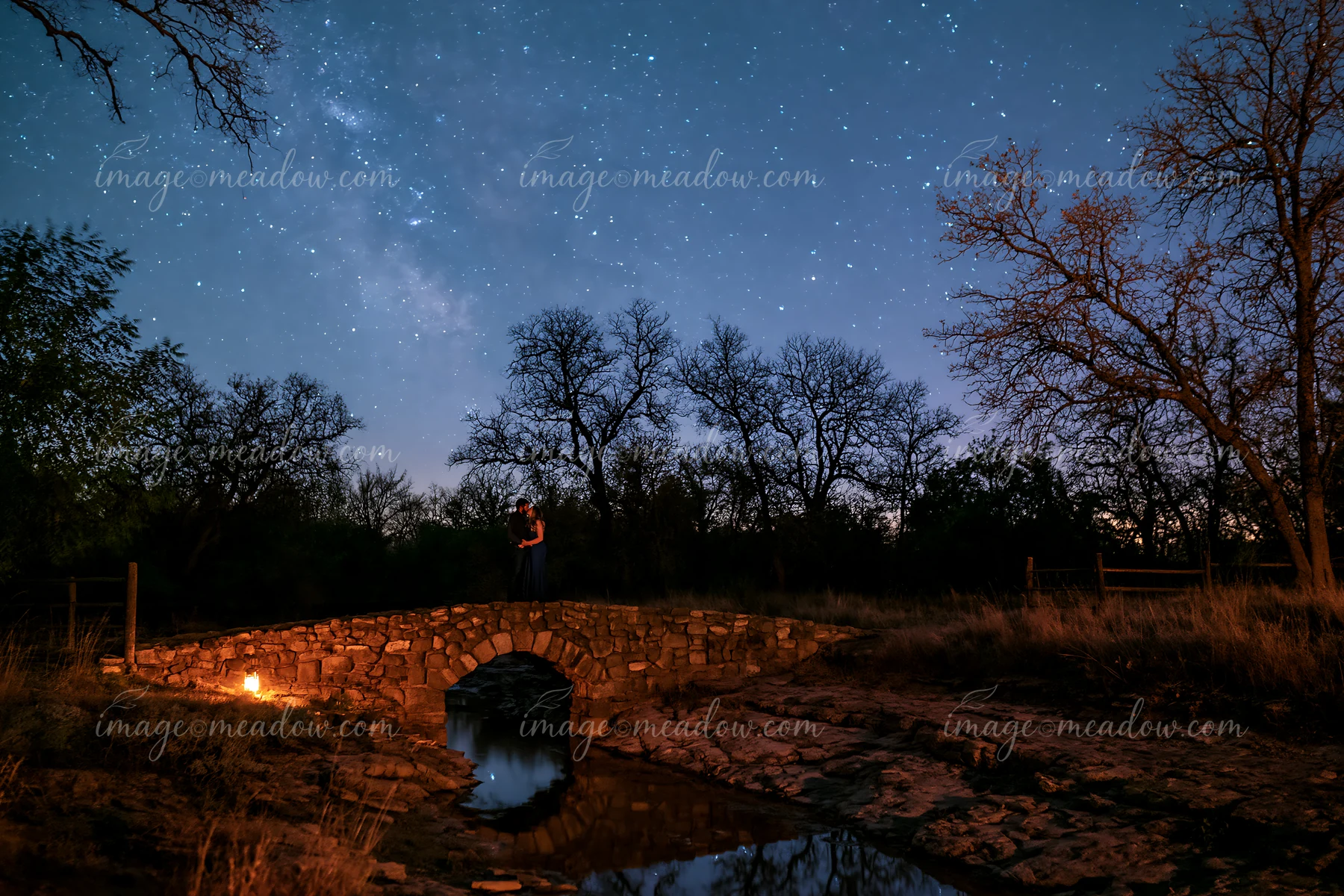 A couple kissing under stars during a romantic date stands on a stone bridge.