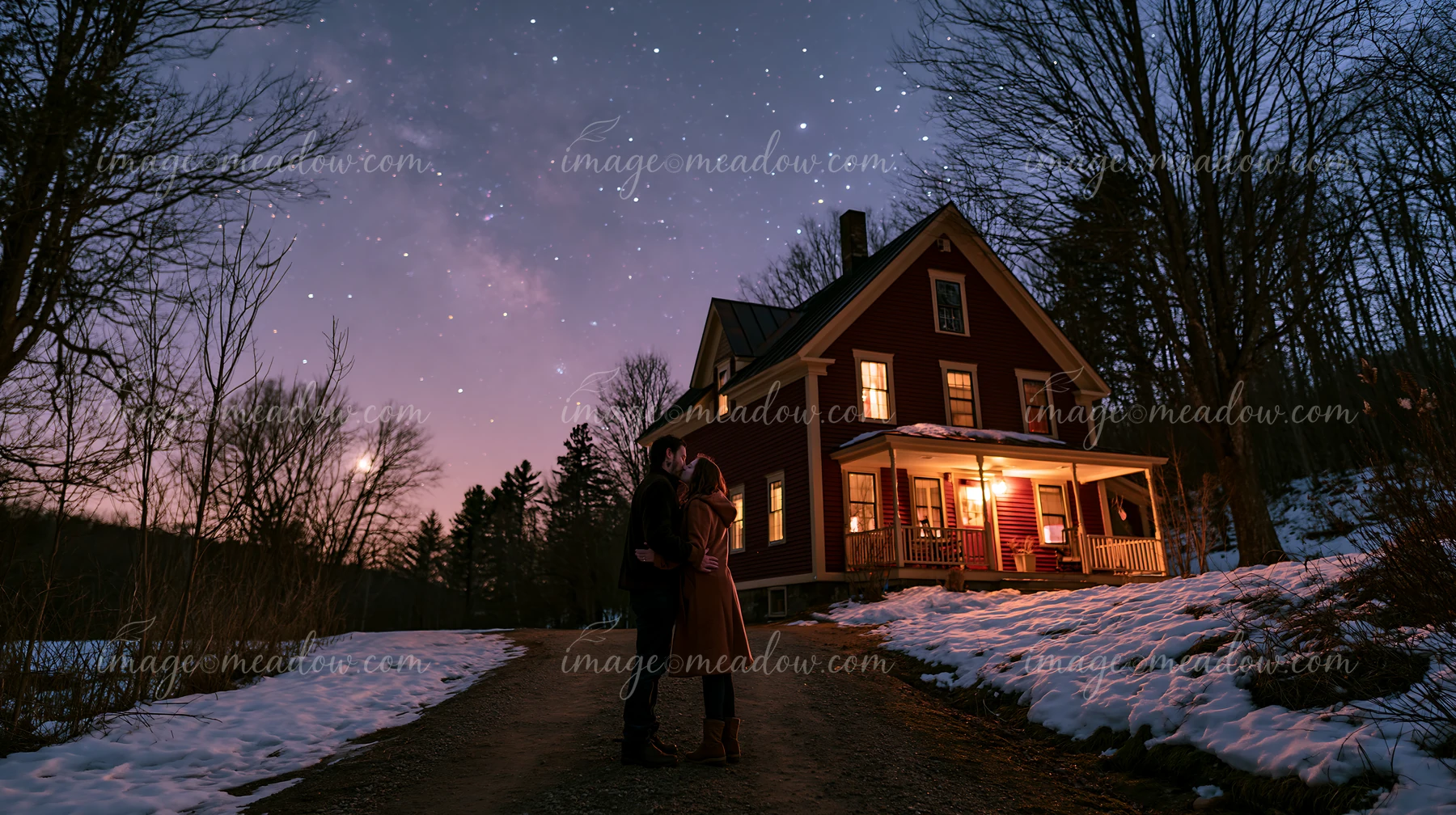 A couple kissing under stars wearing warm coats stands on a path by a cabin.