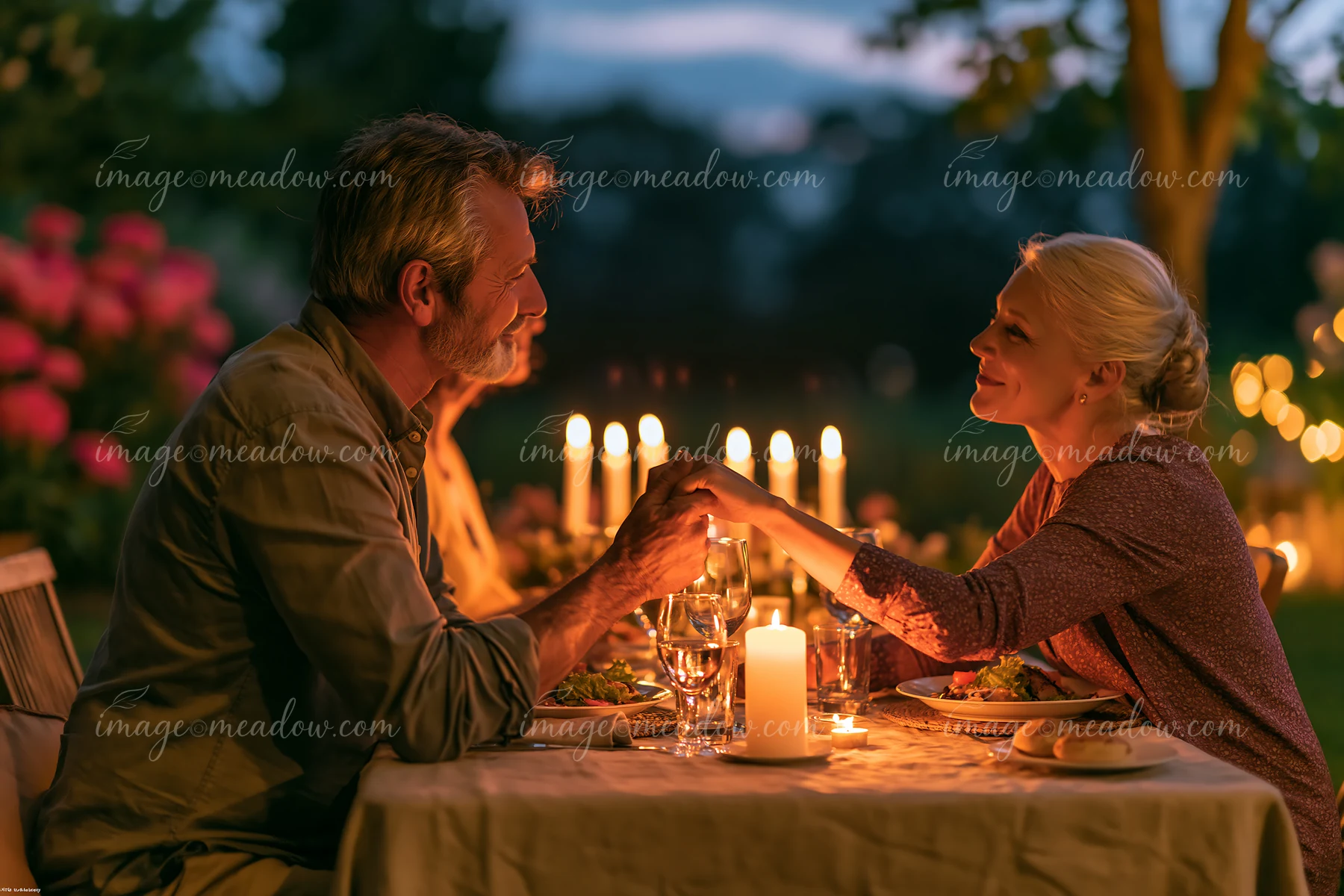 A couple shares a gentle kiss on the hand in a romantic setting during a candlelit dinner.