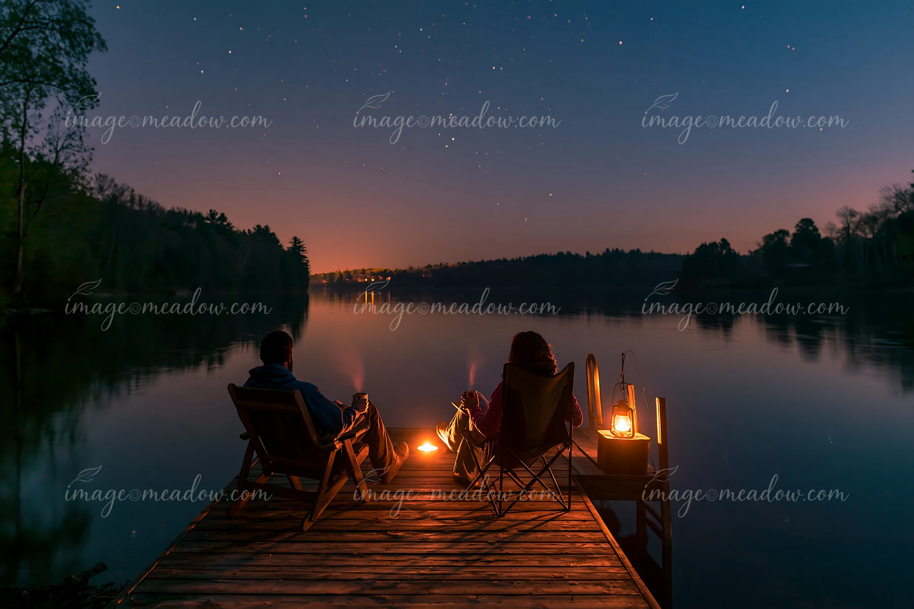 A couple sharing hot drinks under stars sits on a dock by a lake, with a gentle fire illuminating their space.