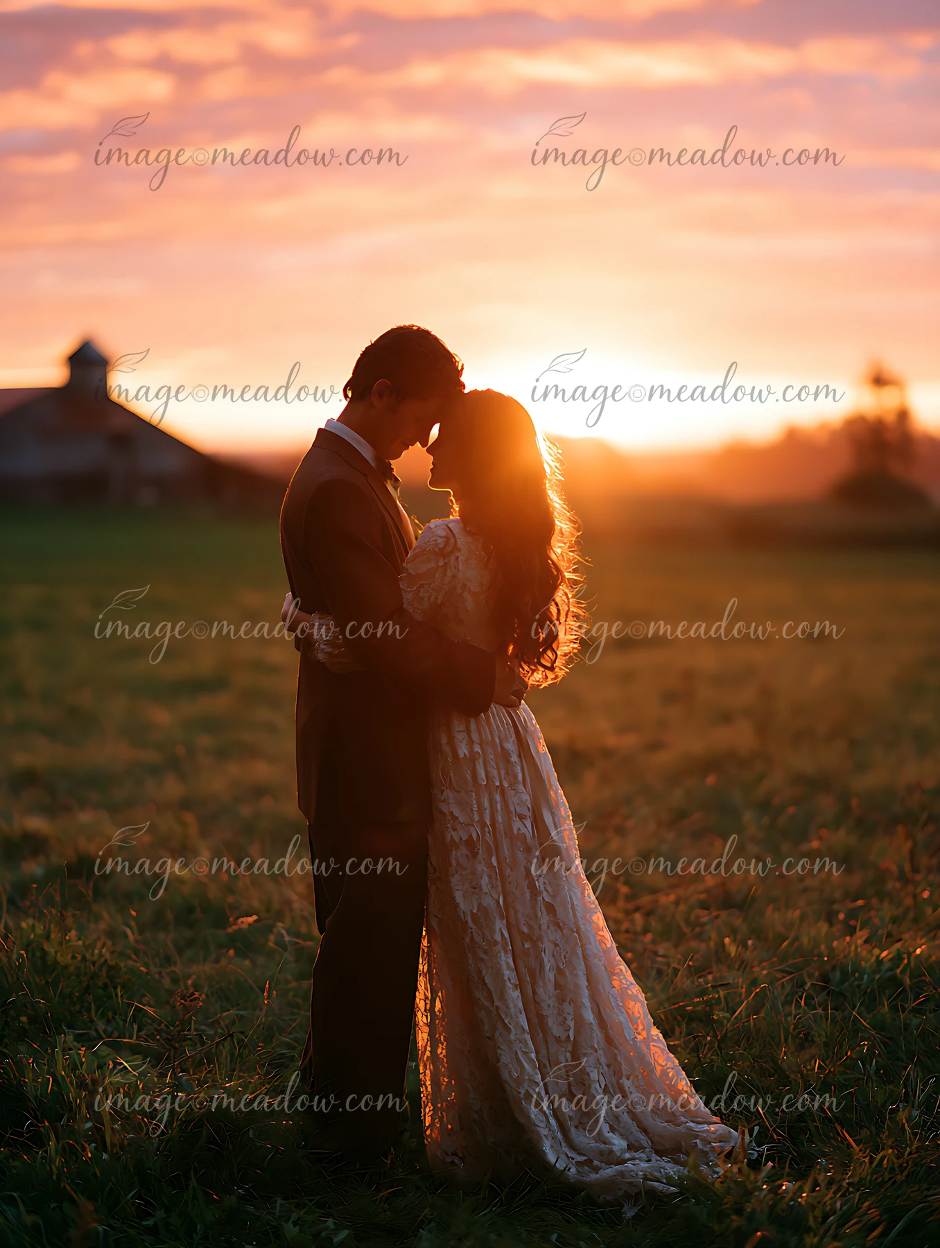 A couple stands close together in an open field at sunset, sharing an intimate moment surrounded by nature and the warm glow of the sun.
