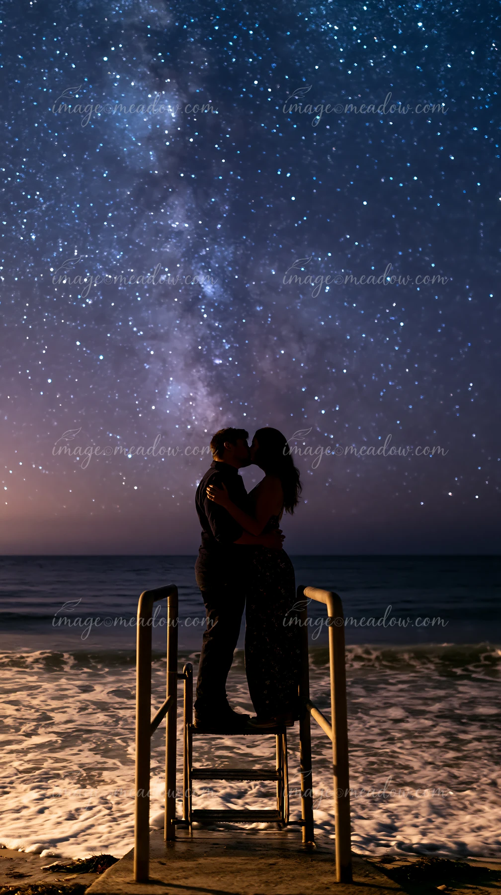 A couple stands on a wooden dock, sharing a romantic kiss under stars near ocean waves.