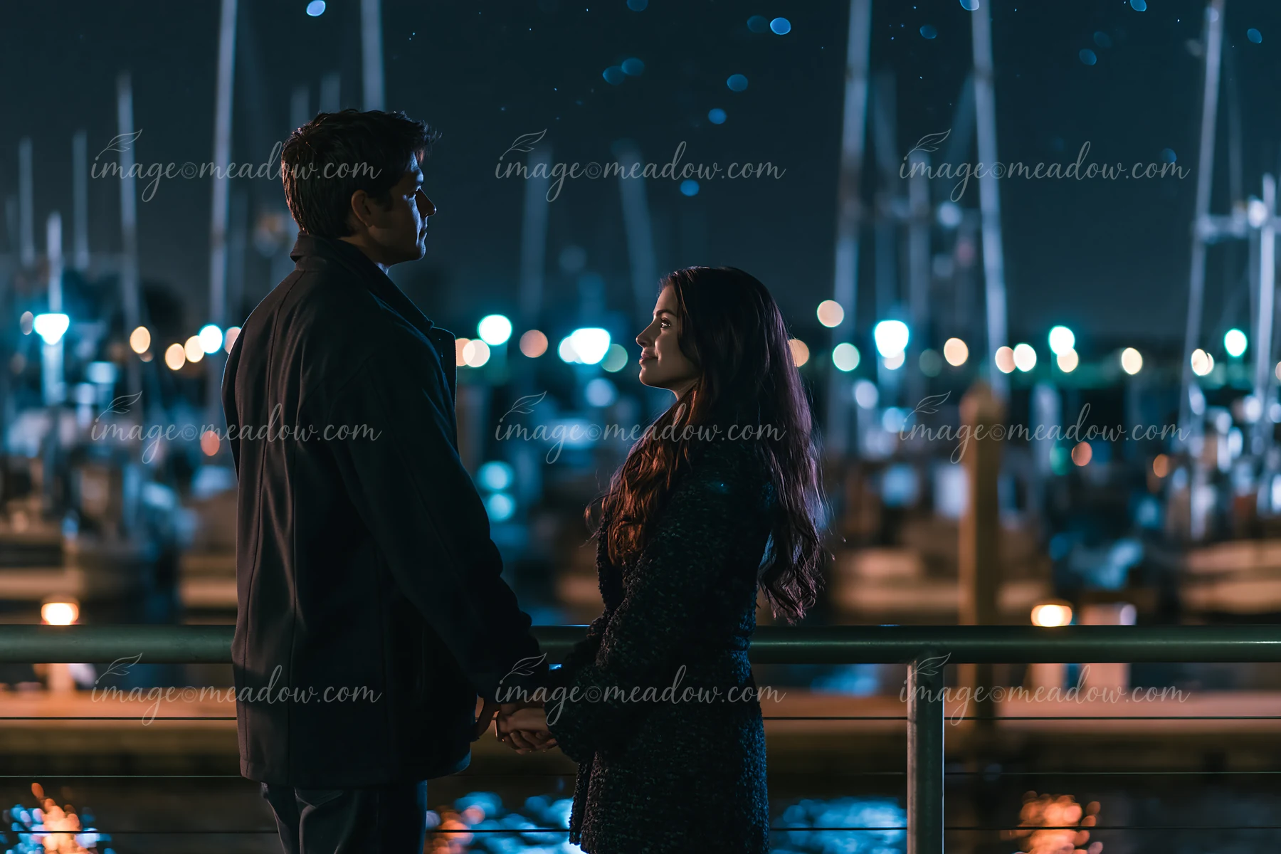 A couple stands together at a marina, holding hands beneath the night sky.