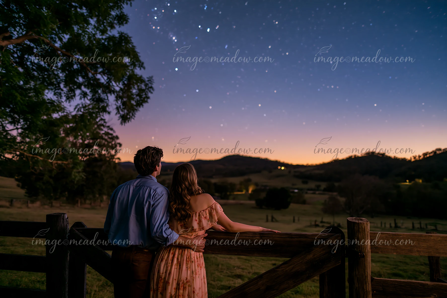 A couple under stars in a rural backyard watches the night sky together.
