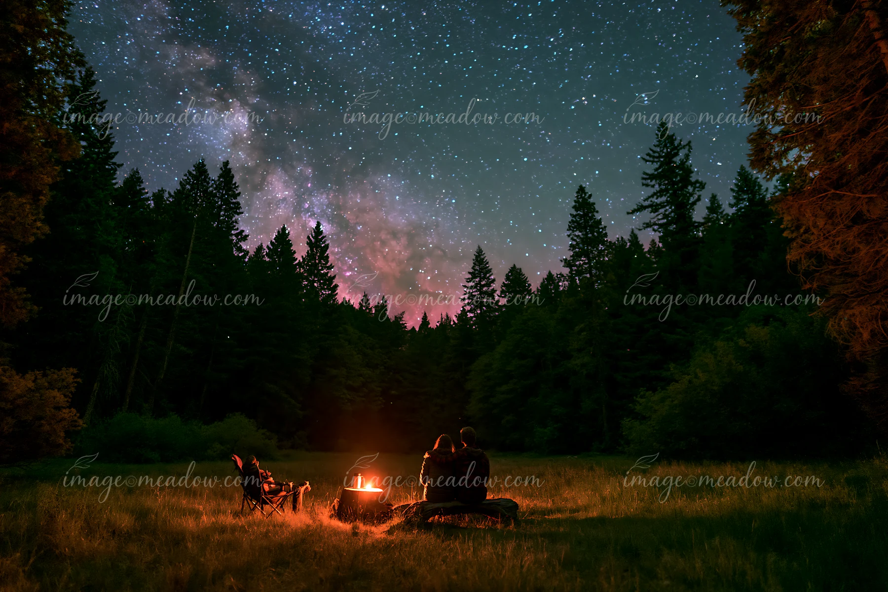 A couple viewing the Milky Way from a forest clearing sits near a campfire under a starry sky, surrounded by tall trees and a peaceful atmosphere.