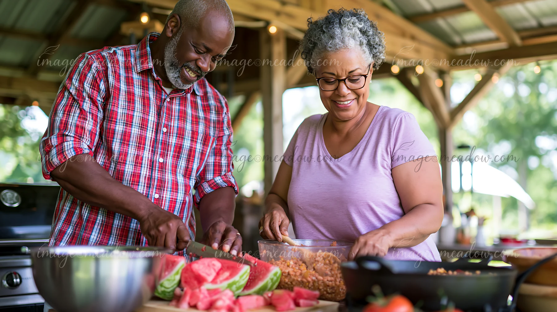 A couple works together to prepare a meal outdoors, chopping vegetables and enjoying each other's company.