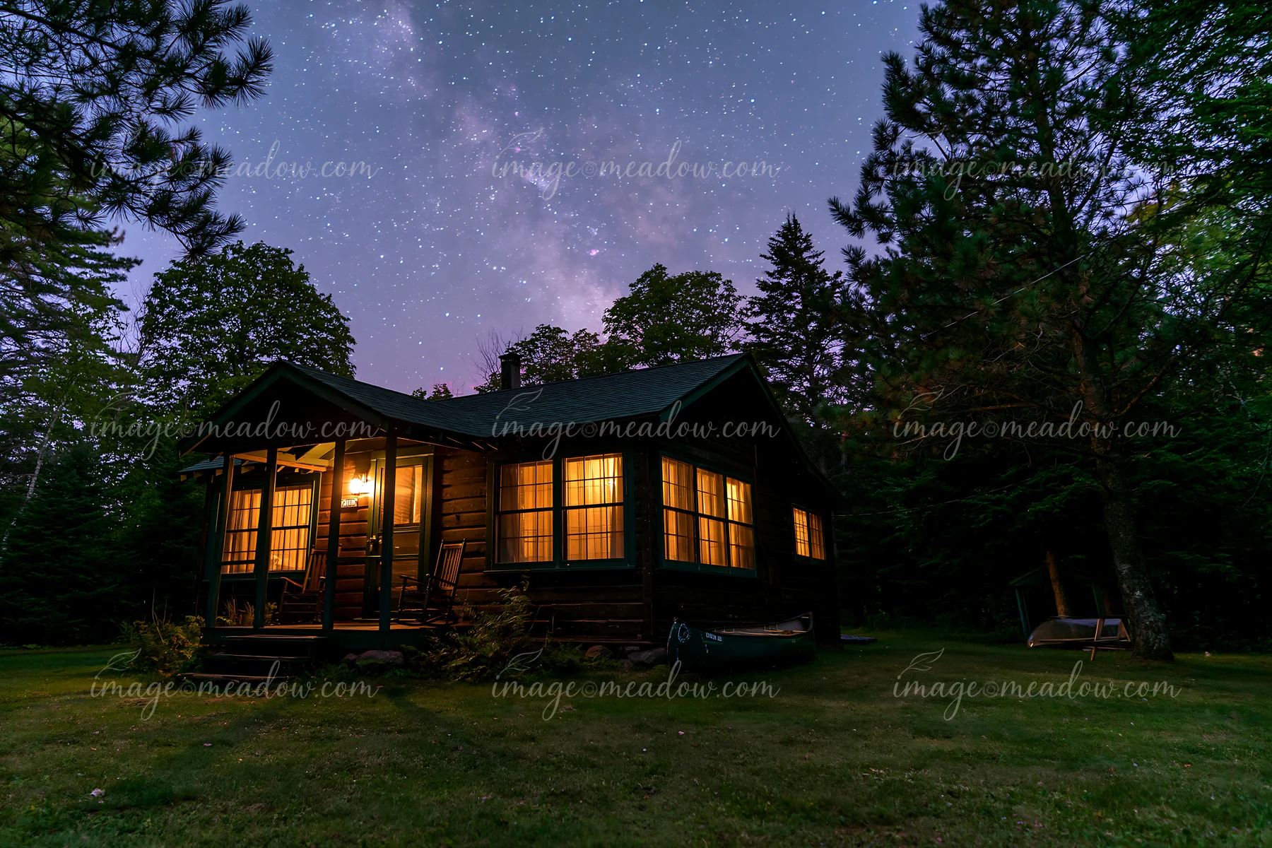 A cozy holiday home under stars stands in a forest, with warm lights glowing from its windows.