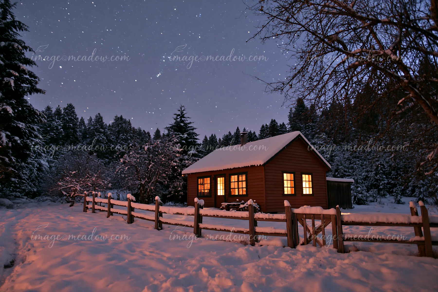 A cozy house sits in a snowy landscape with warm light glowing from its windows.