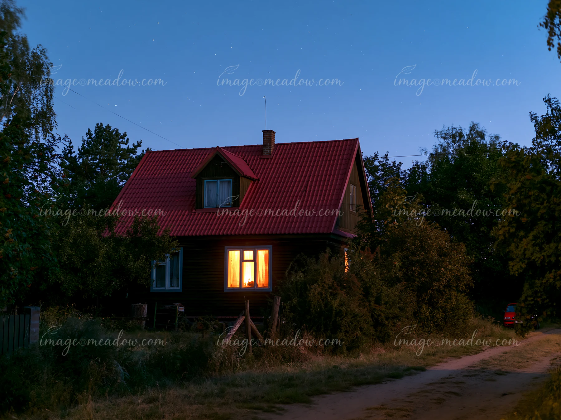 A cozy house stands illuminated at dusk, surrounded by trees and shrubs.