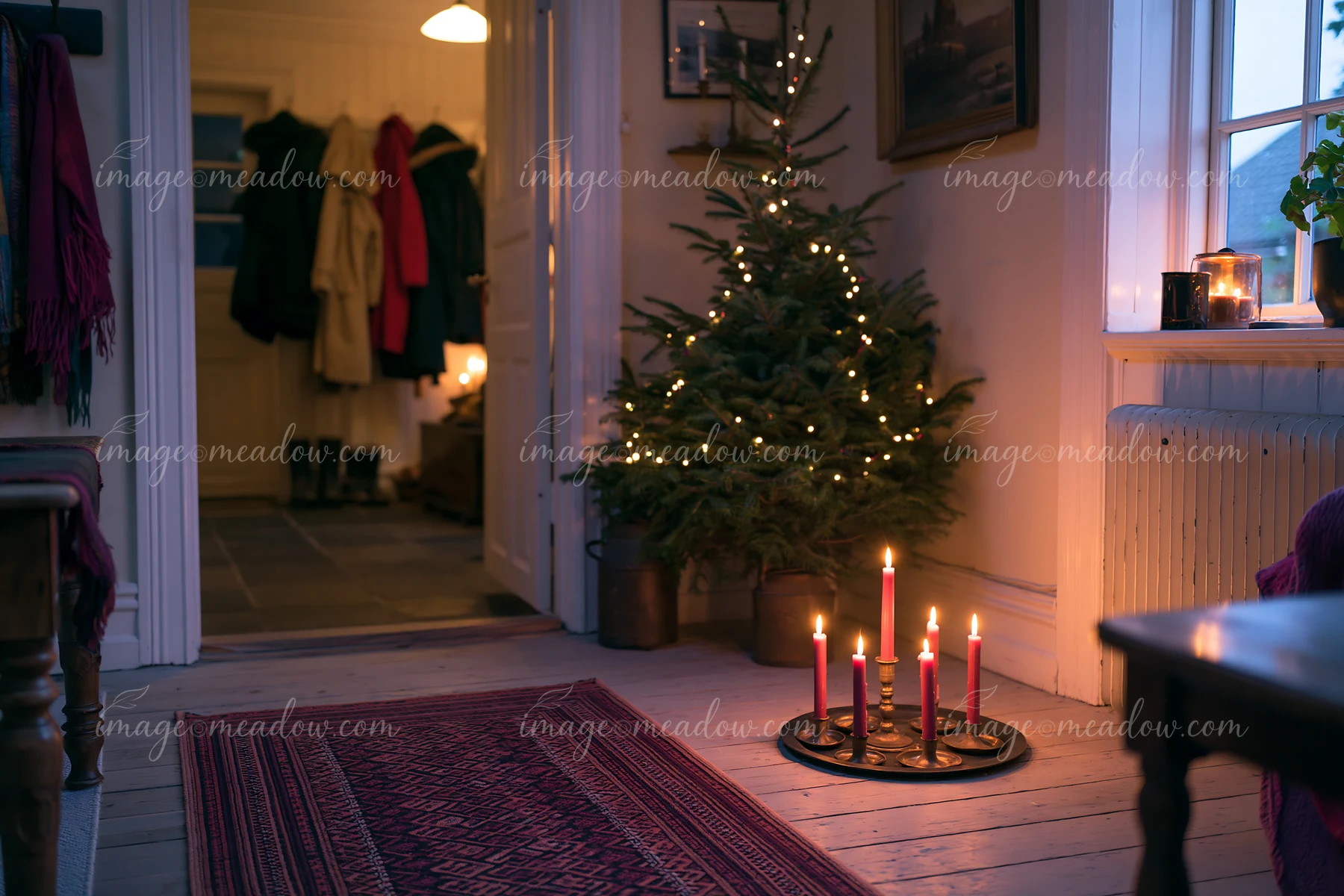 A cozy living room features a lit Christmas tree and glowing candles on a stand.