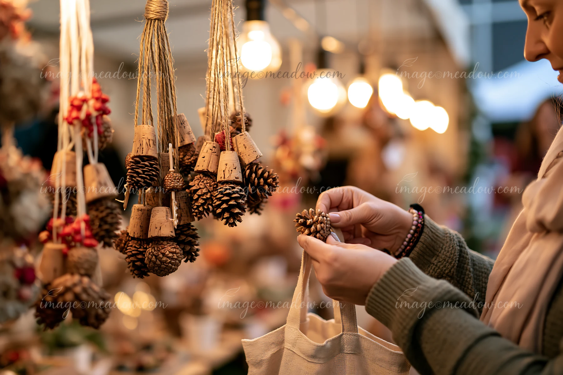 A customer examines a handmade ornament at a bustling Christmas market stall filled with decorative items.