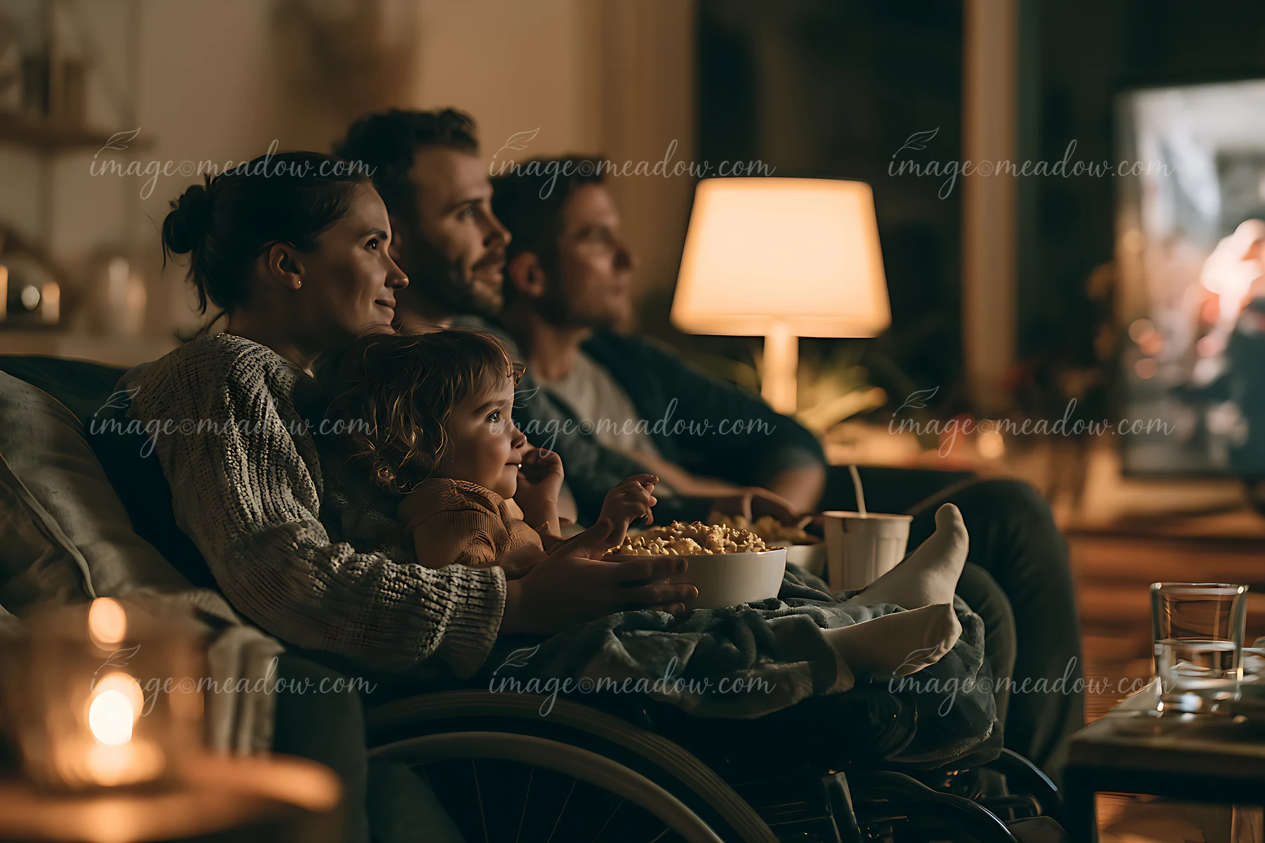 A family enjoys a movie night at home while sitting on a couch, with snacks in hand.