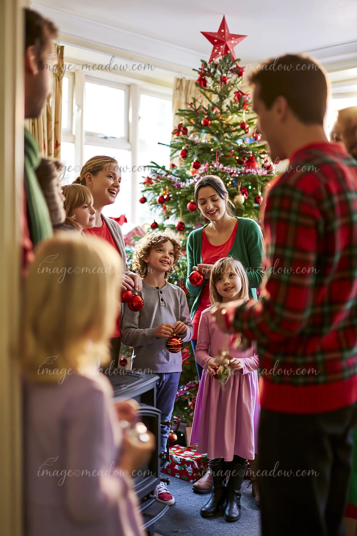 A family is singing Christmas carols together indoors, surrounded by festive decorations and a Christmas tree.