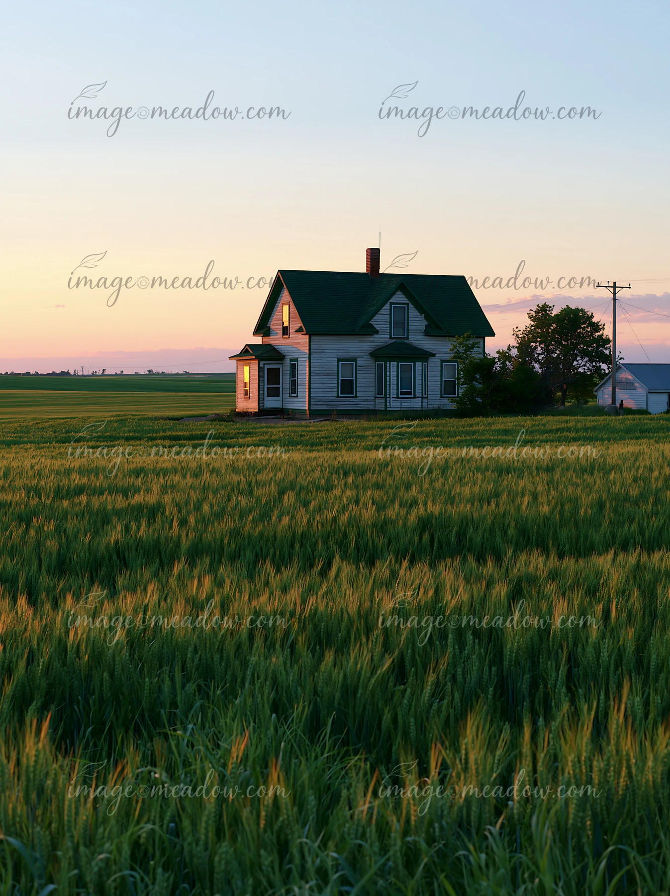 A farmhouse among green fields stands at dusk with soft light illuminating the windows.