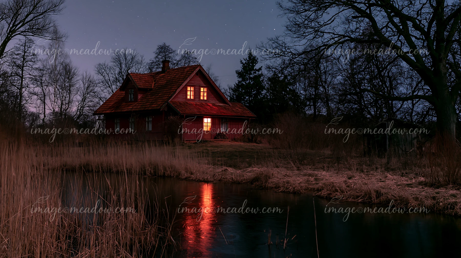 A farmhouse beneath night sky stands near a calm water body.