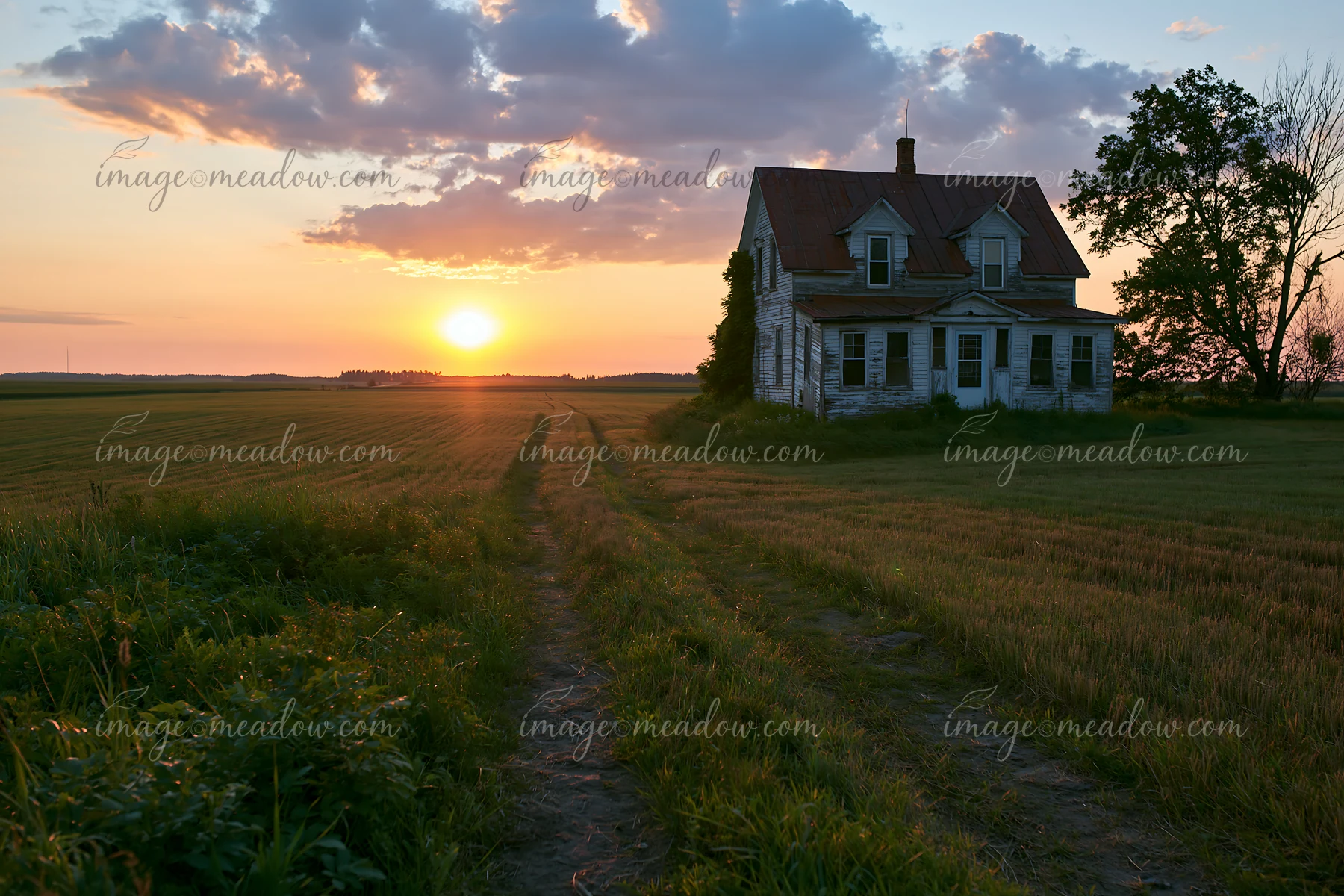 A farmhouse stands near a dirt road as the sun sets over open fields.